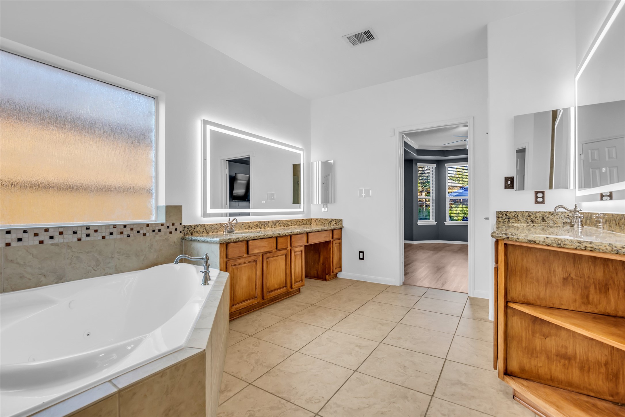 Spacious primary bathroom featuring a luxurious soaking tub, dual vanities with granite countertops, and elegant tile flooring.