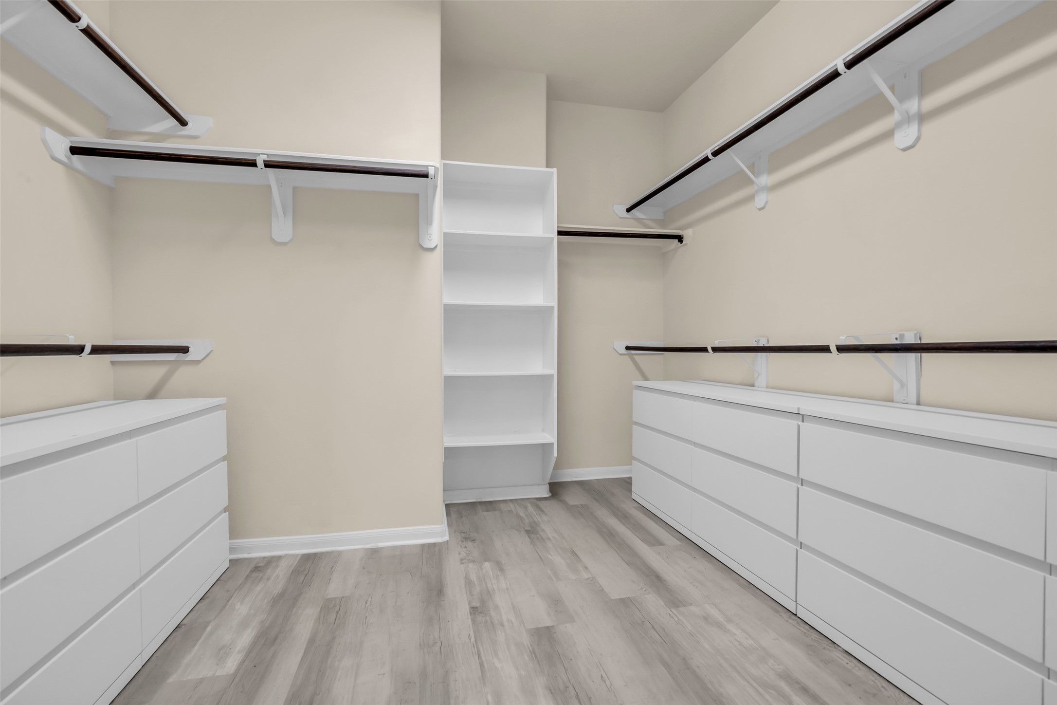 Spacious walk-in closet featuring ample shelving, multiple hanging rods, and sleek white cabinetry for organized storage.