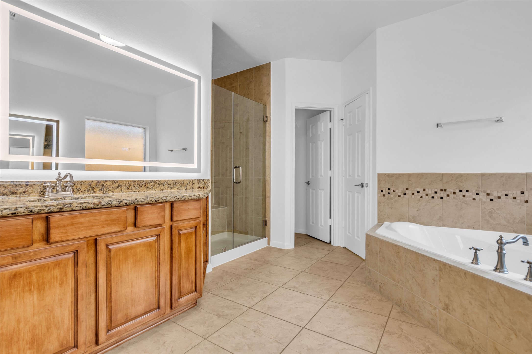 Spacious bathroom featuring a granite-topped vanity with ample storage, a luxurious soaking tub, and a modern glass-enclosed shower.