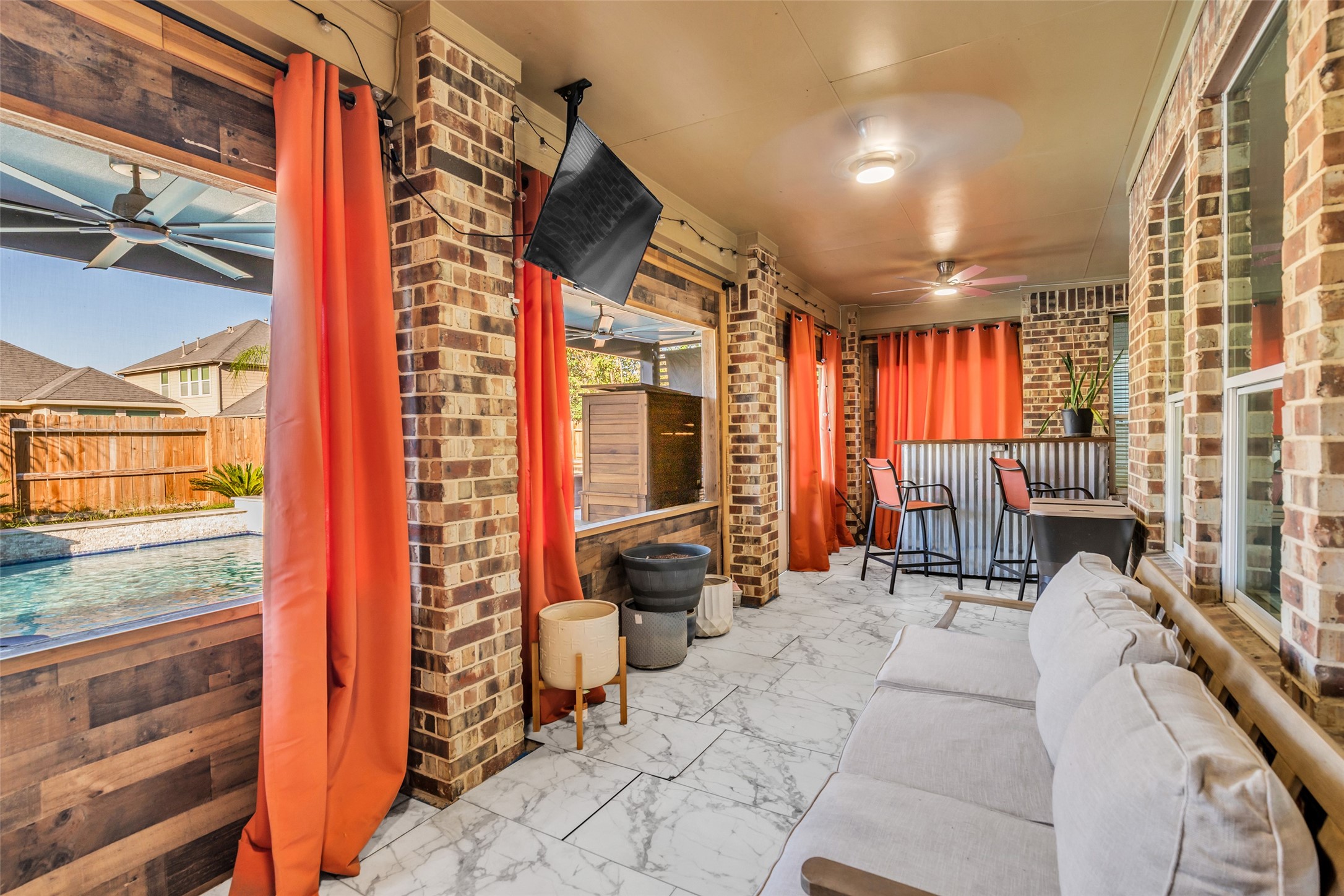 Charming sunroom with brick accents, vibrant orange curtains, and a view of the pool. Enjoy relaxing on the comfortable seating or entertaining at the bar area.