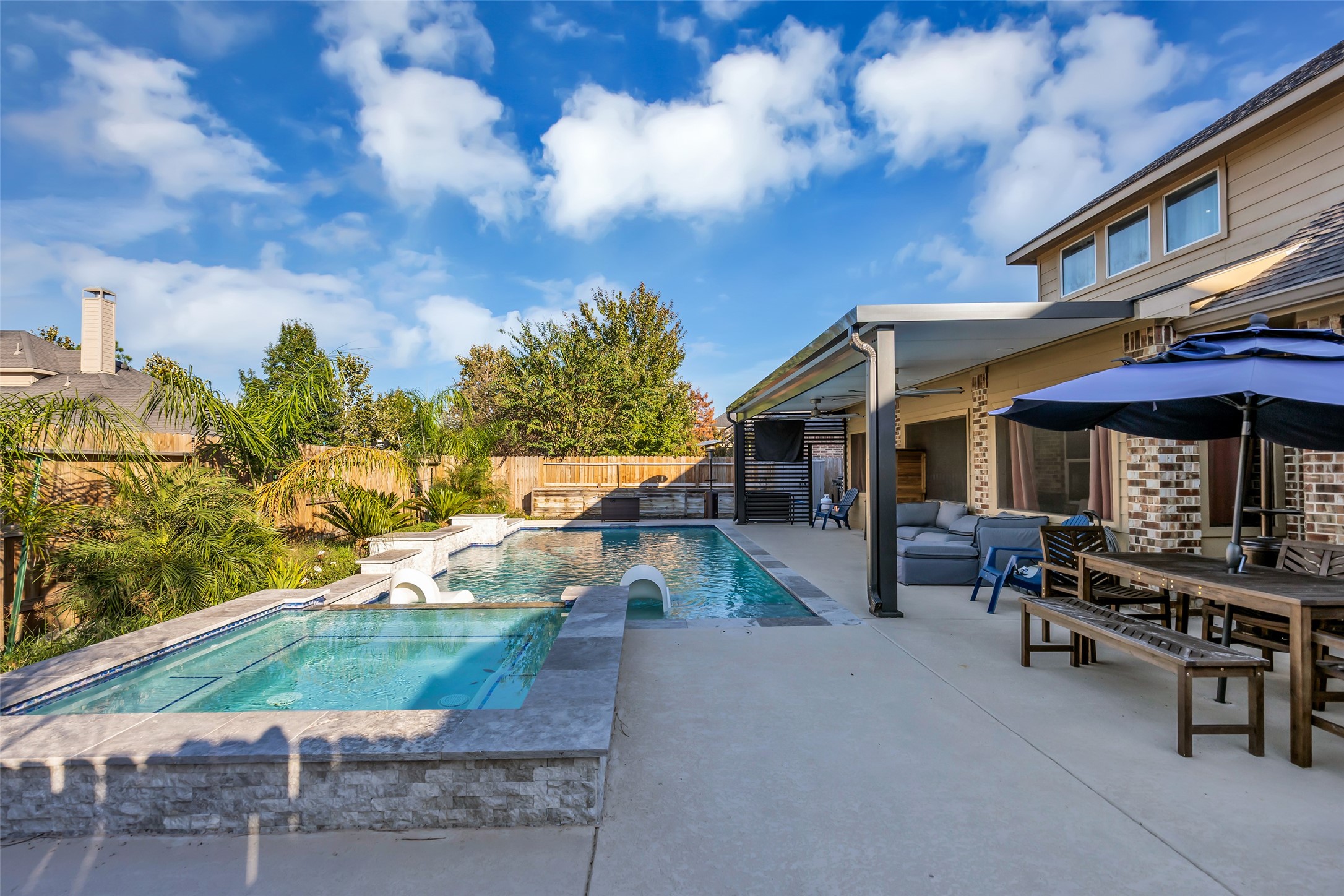 Stunning backyard oasis featuring a luxurious swimming pool and spa, complemented by a spacious patio with ample seating and dining space under a stylish pergola.