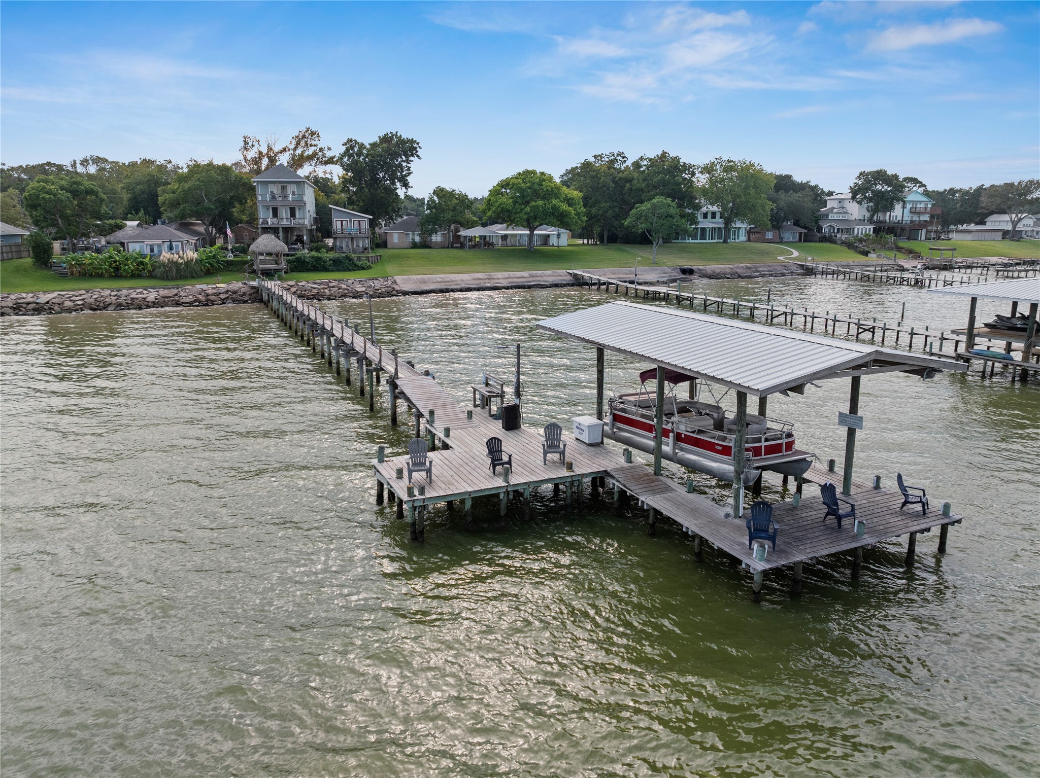 This waterfront property features a long pier leading to a spacious dock with seating and a covered boat area, offering serene views and direct access to the water.