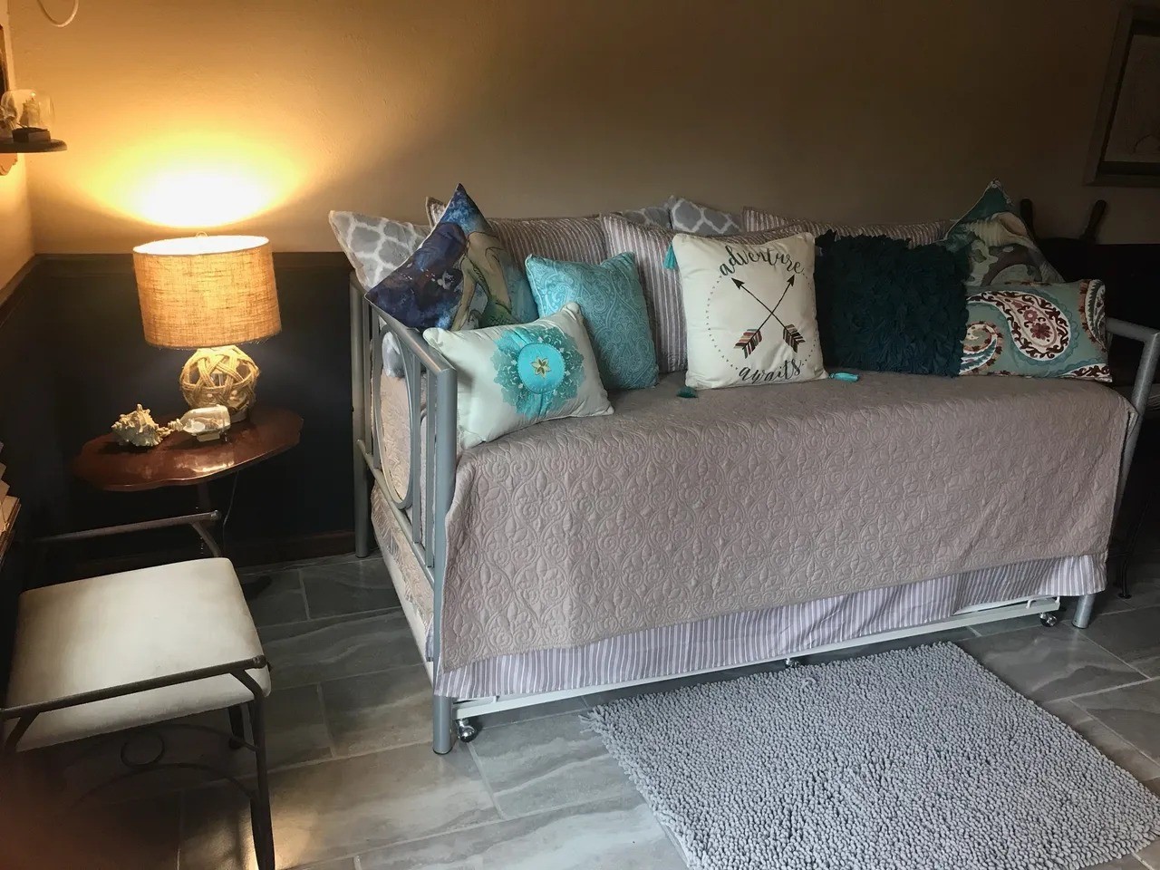 Welcome to the Captain's Quartersa cozy retreat featuring a stylish daybed adorned with plush, nautical-themed pillows. Soft lighting and charming seaside decor create a warm, inviting atmosphere perfect for relaxation.