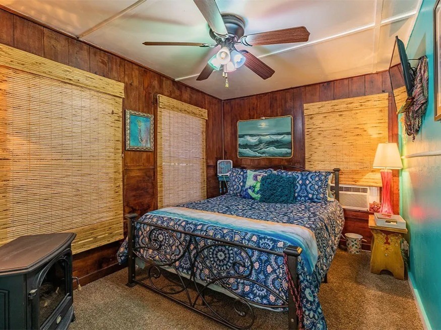 Cozy and inviting bedroom in the Saltwater Gypsy with a nautical theme, featuring warm wood paneling, vibrant decor, and a ceiling fan for comfort. Perfect for a tranquil retreat.