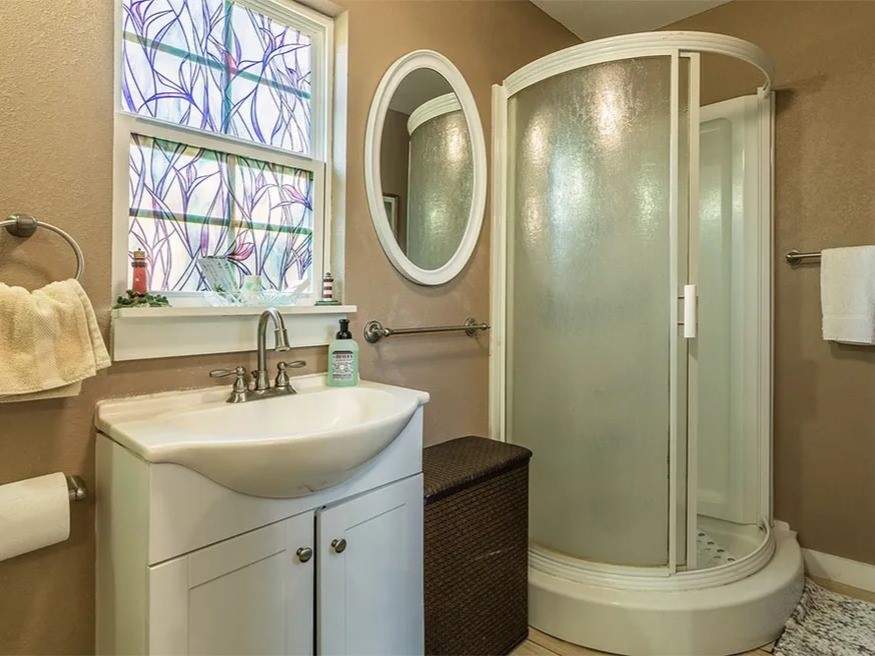 Charming bathroom in the Doc Holiday with a stylish round shower, elegant oval mirror, and inviting natural light through decorative windows. Perfect for relaxation.