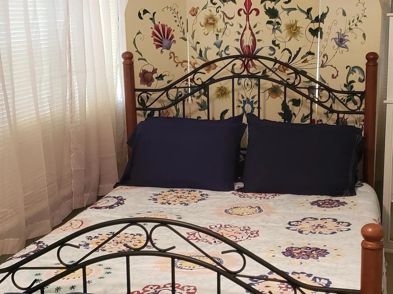 Charming bedroom in the Laurel Anne featuring a decorative wrought iron bed frame, vibrant floral accents, and abundant natural light. Perfect for a cozy retreat.
