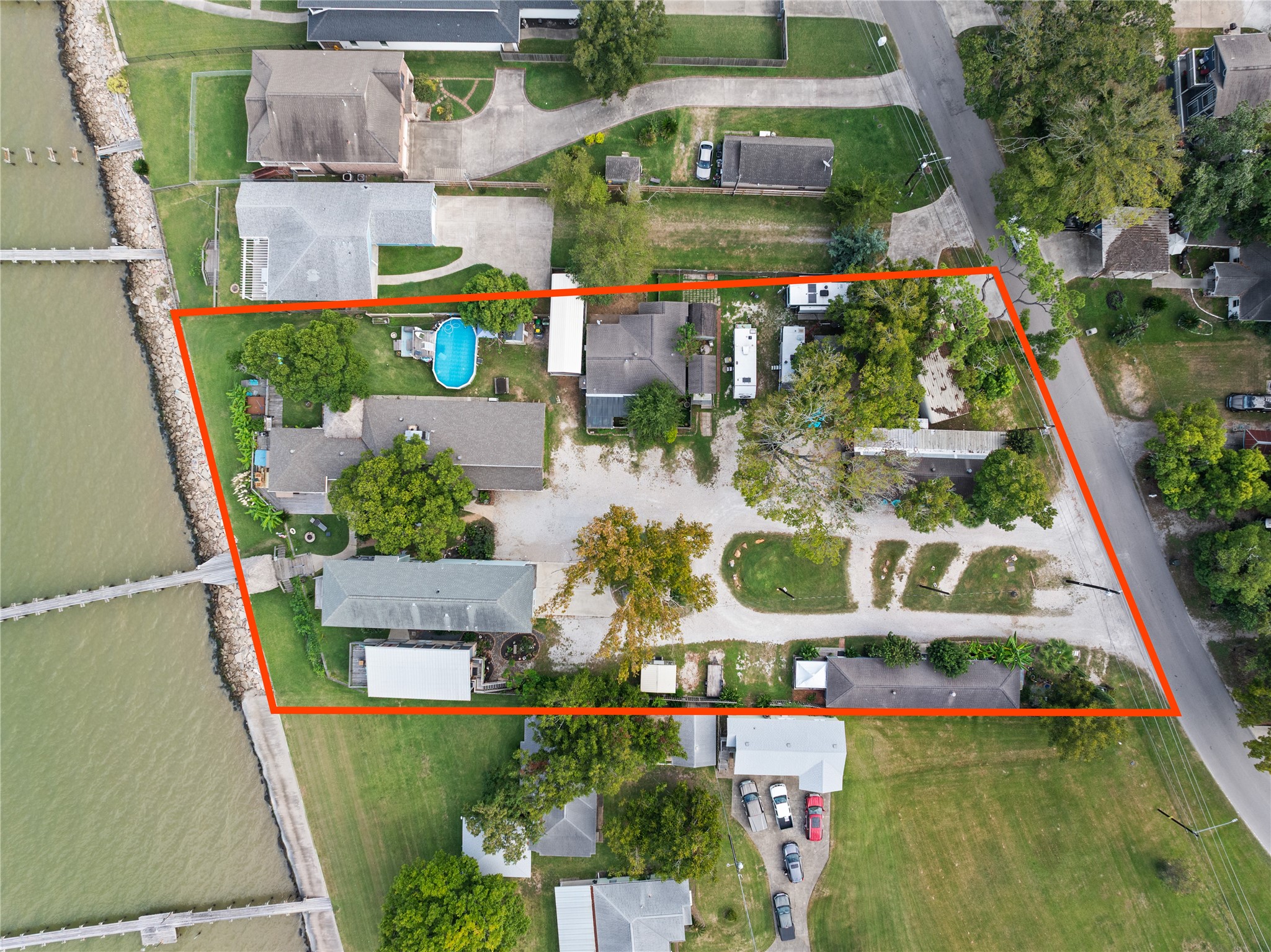 This aerial photo shows the waterfront property bordered in red, featuring multiple buildings and mature trees. It has direct water access, a spacious layout, and is adjacent to a quiet neighborhood street.