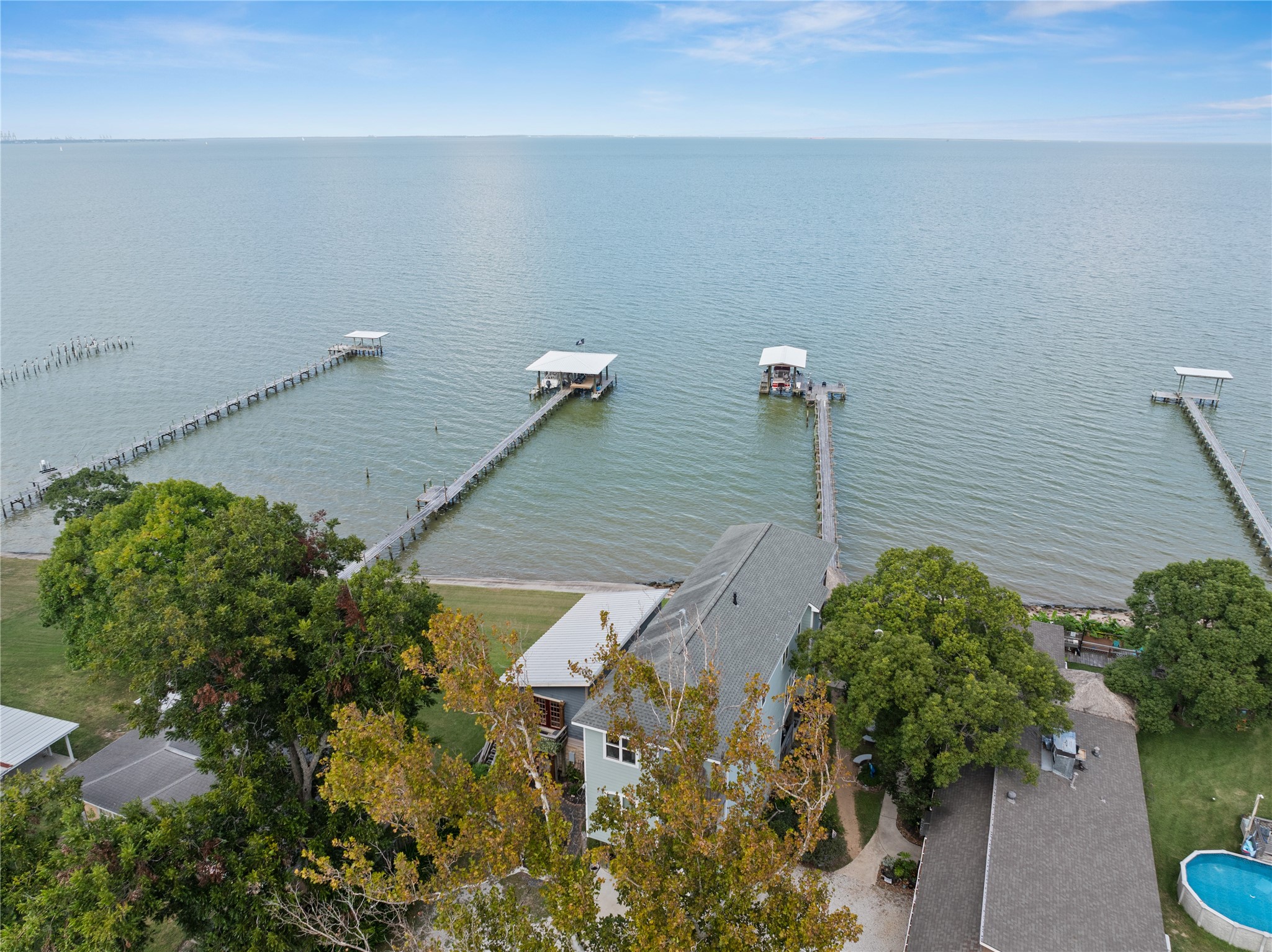 This waterfront property is nestled among lush trees with direct access to a private pier extending into calm waters, offering stunning views and serene living by the bay.