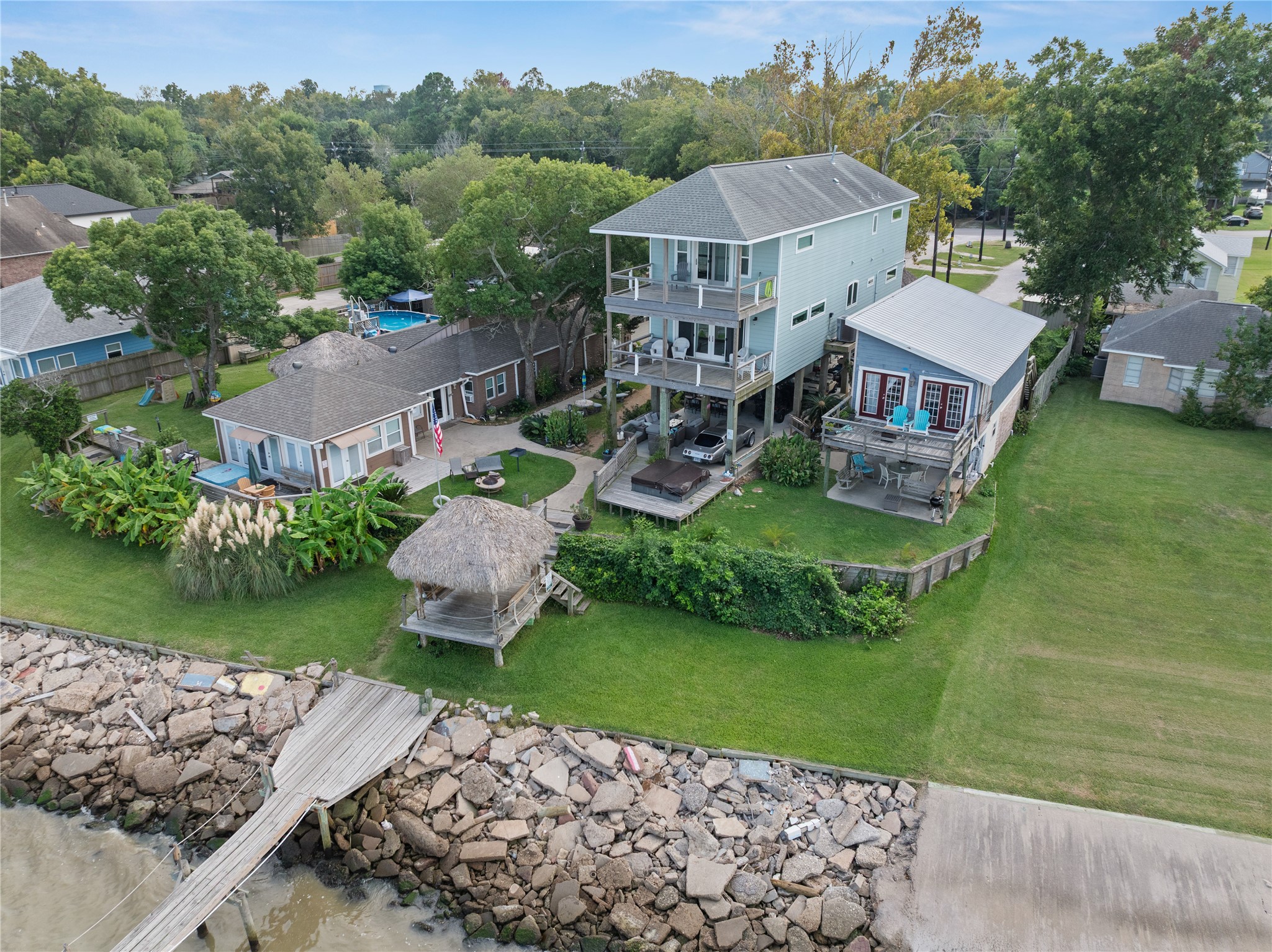 This photo is from the waterfront showing the subject property and three homes with multiple balconies overlooking the water. The backyard includes a lush lawn, tropical landscaping, and a thatched-roof gazebo. A pier extends to the water, perfect for boating enthusiasts. This photo is from the waterfront showing the subject property and three homes with multiple balconies overlooking the water. The backyard includes a lush lawn, tropical landscaping, and a thatched-roof gazebo. A pier extends to the water, perfect for boating enthusiasts.