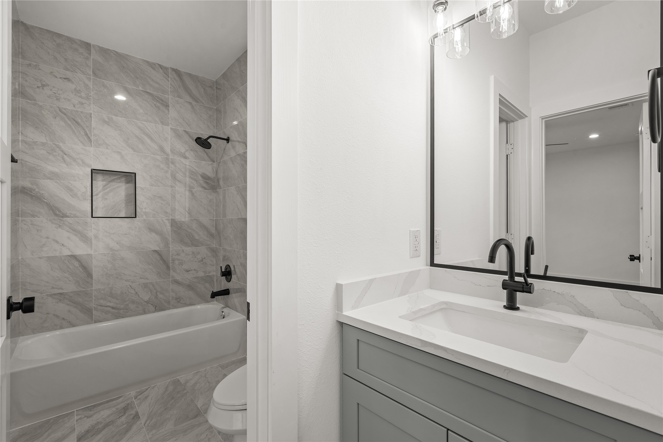 The secondary bath is finished with floor-to-ceiling marble-look tile around the tub-shower combination, a
built-in niche, and a quartz-topped vanity with the matte-black fixtures carried throughout the home.
