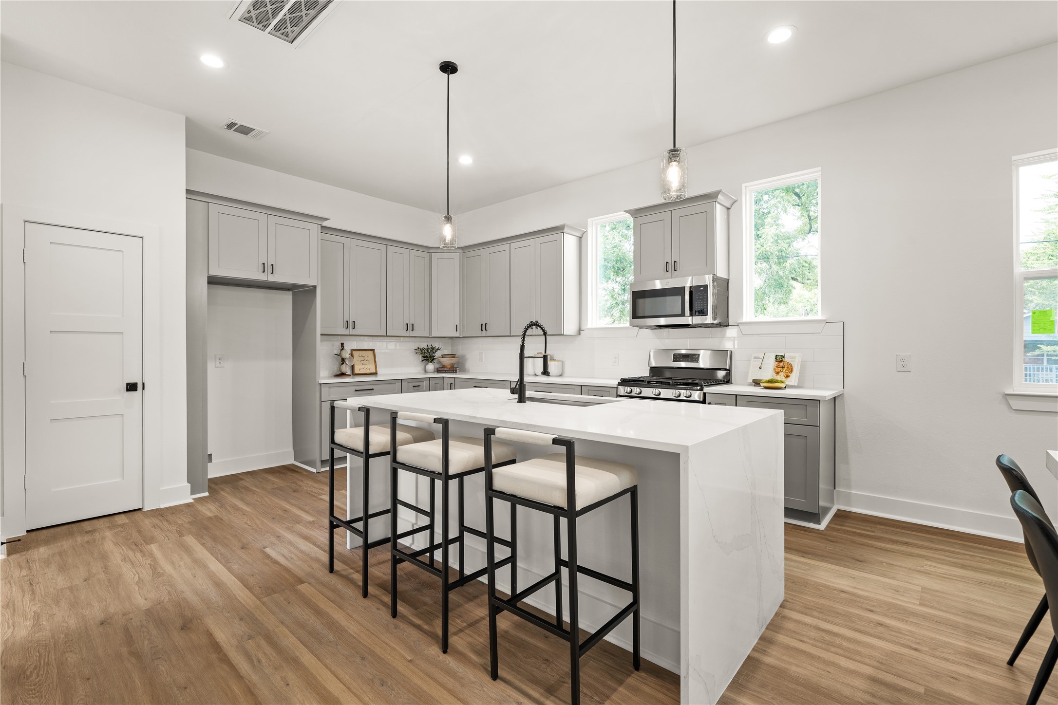 The kitchen makes an immediate statement with a waterfall-edge island, gray Shaker cabinetry with
matte-black hardware, and seeded-glass pendants, creating a natural centerpiece for cooking, gathering, and
lingering.