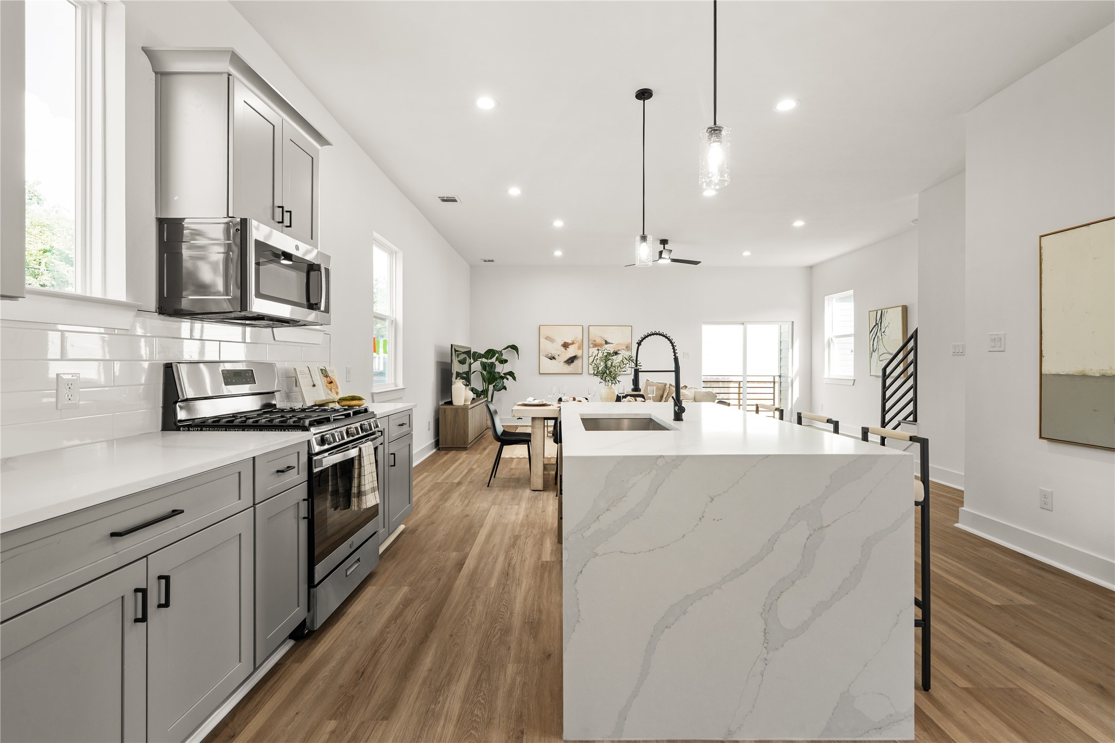 The quartz waterfall island features distinctive veining that cascades along its sides, adding visual interest
while creating a seamless connection to the dining and living areas.