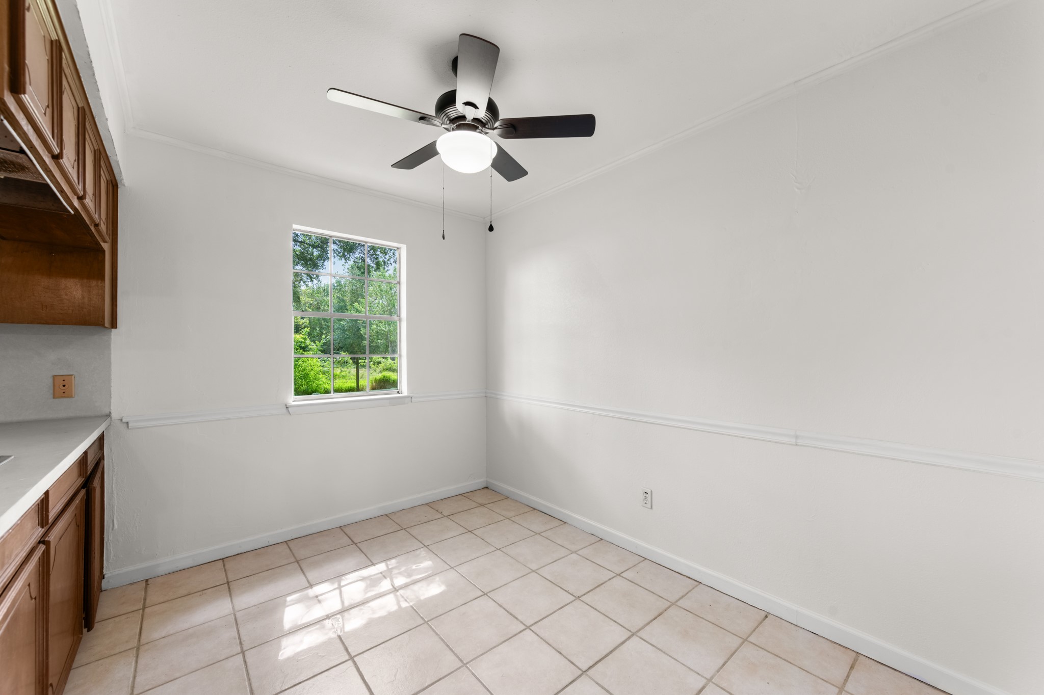 Bright dining area featuring tile flooring, chair rail molding, a ceiling fan, and a window overlooking the greenery outside. A welcoming space for everyday meals and gatherings.