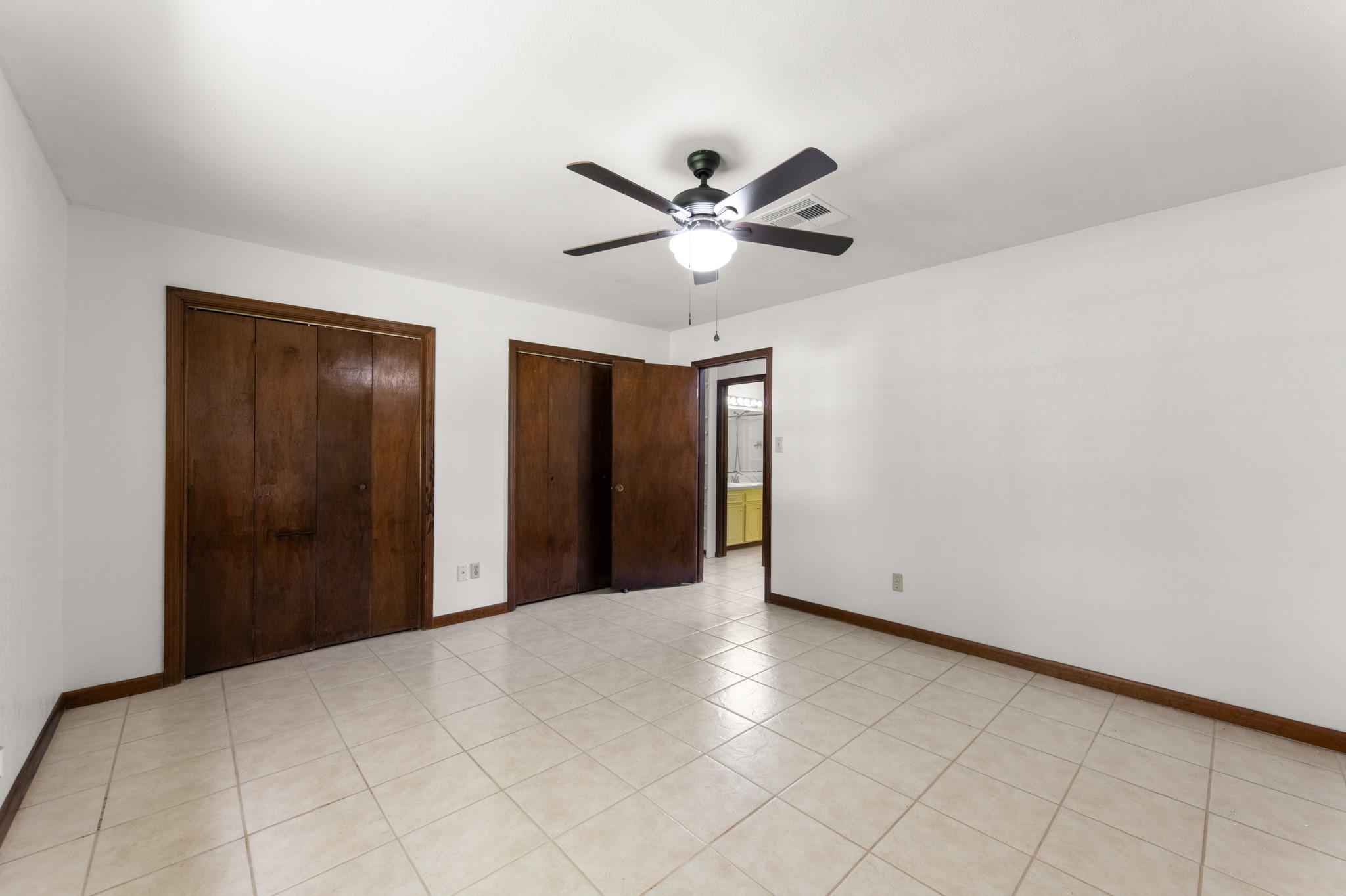 Another view of the primary suite highlights two closets, a ceiling fan, and convenient access to the adjoining bathroom.
