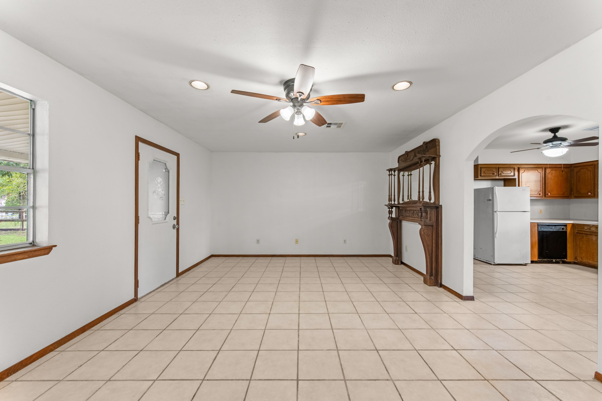 Another perspective showcases the living room's open floor space, decorative wood mantel, and convenient connection to the kitchen through a charming arched doorway.