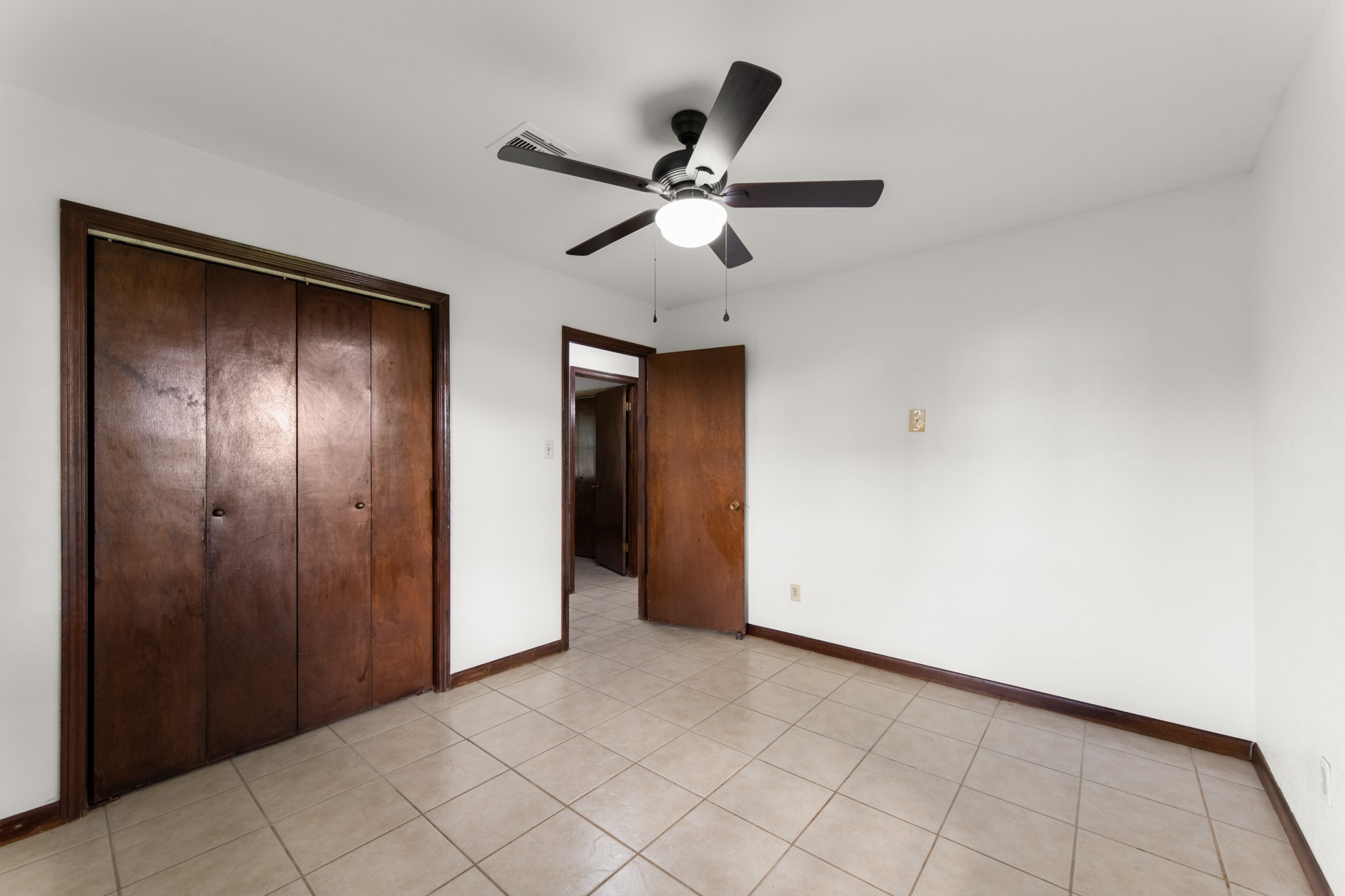 Another perspective highlighting the bedroom's generous closet space, rich wood trim, tile flooring, and ceiling fan.