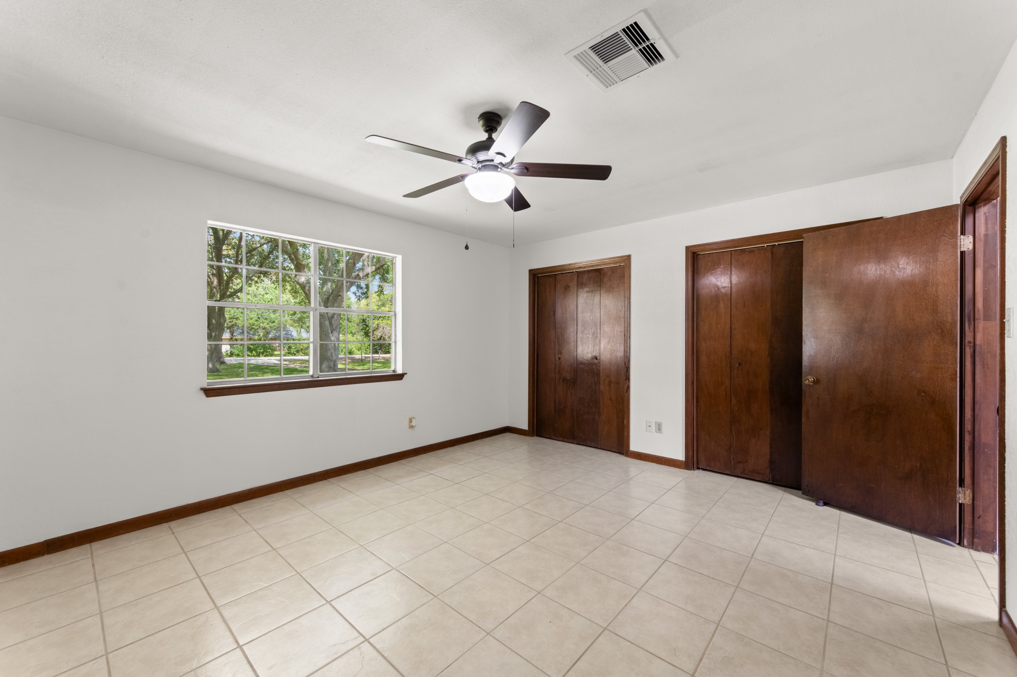 Natural light fills the primary bedroom, with views of mature trees, warm wood trim, and generous closet space.