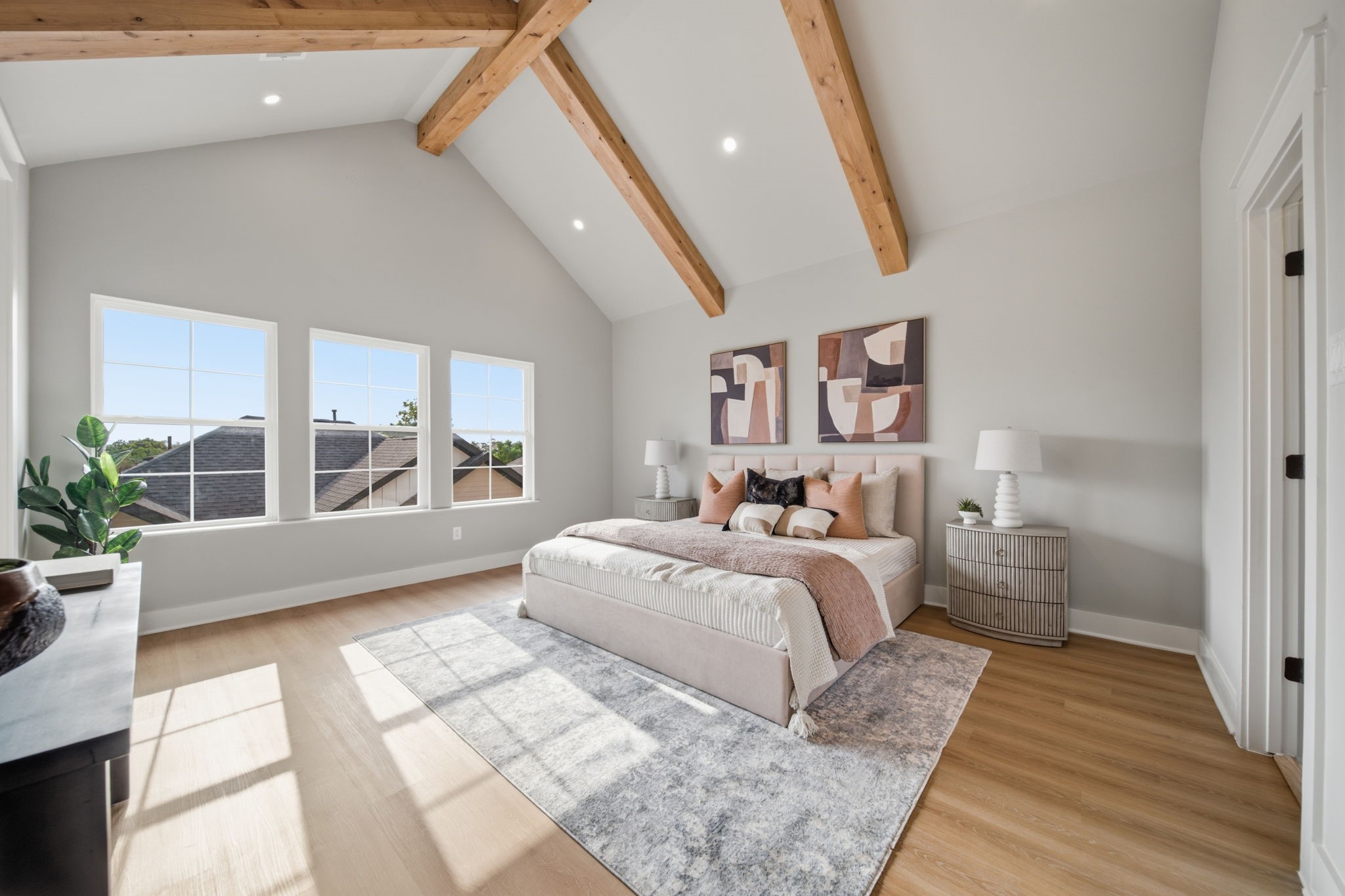 Spacious and bright primary bedroom with wood beams and recessed lighting.