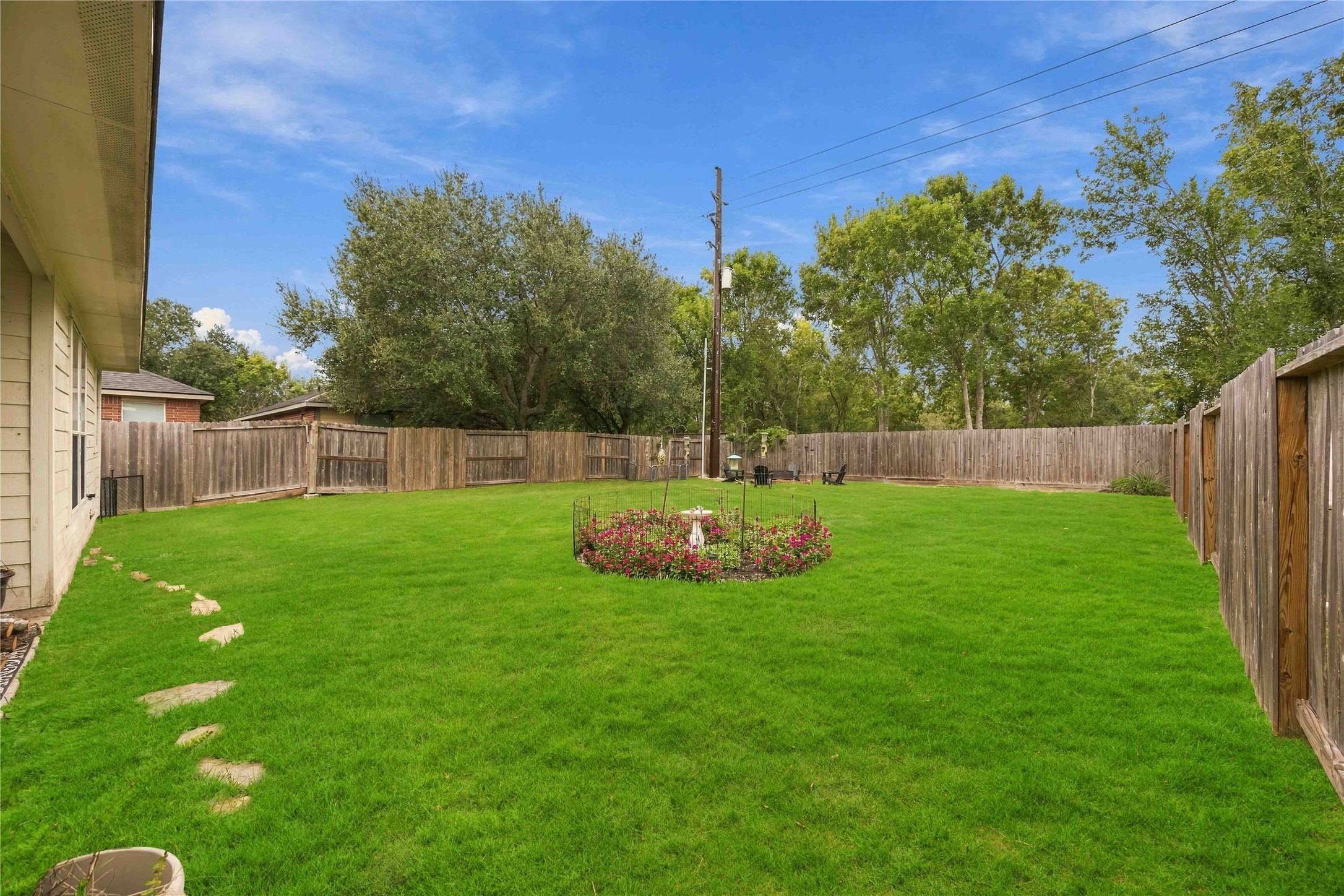 Generously sized backyard with a lush green lawn, perimeter wood fencing, and landscaped garden bed.