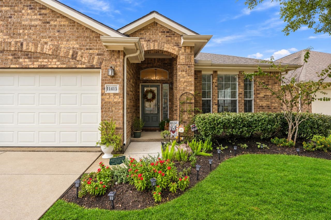 Covered front entry framed by classic brickwork, landscaped flower beds, and large windows.