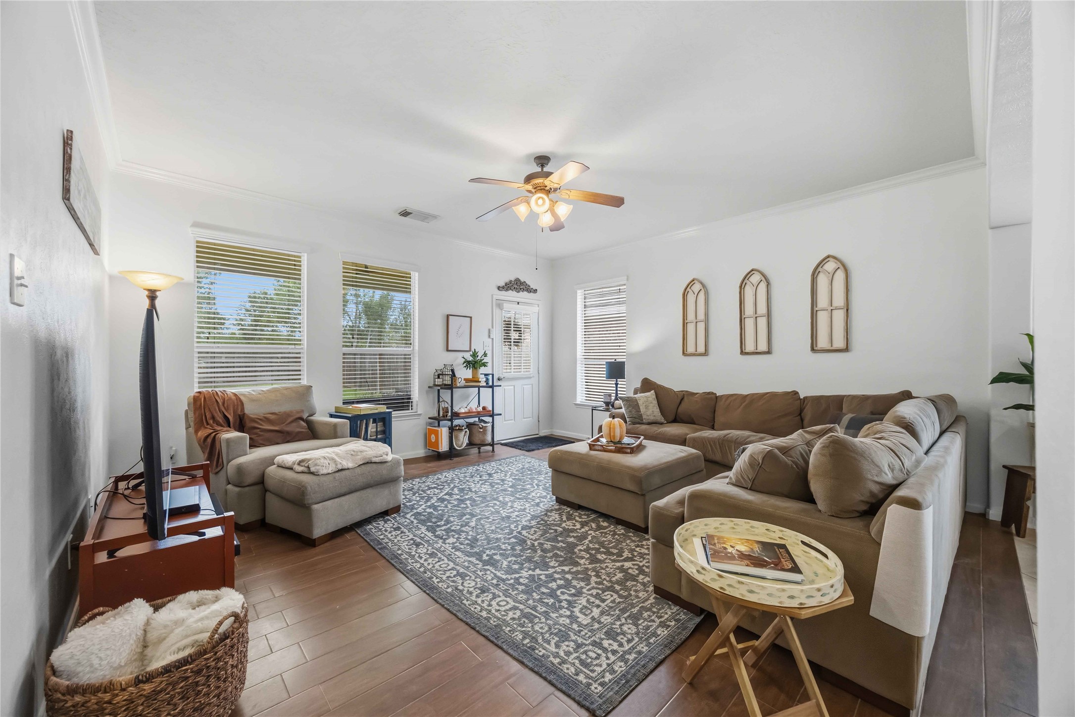 Spacious family room featuring wood-look tile flooring, crown molding, and large windows that bring in natural light.