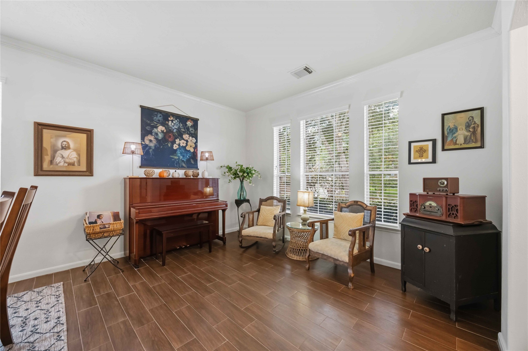 Versatile front living area with wood-look tile flooring, crown molding, and three large windows providing natural light.
