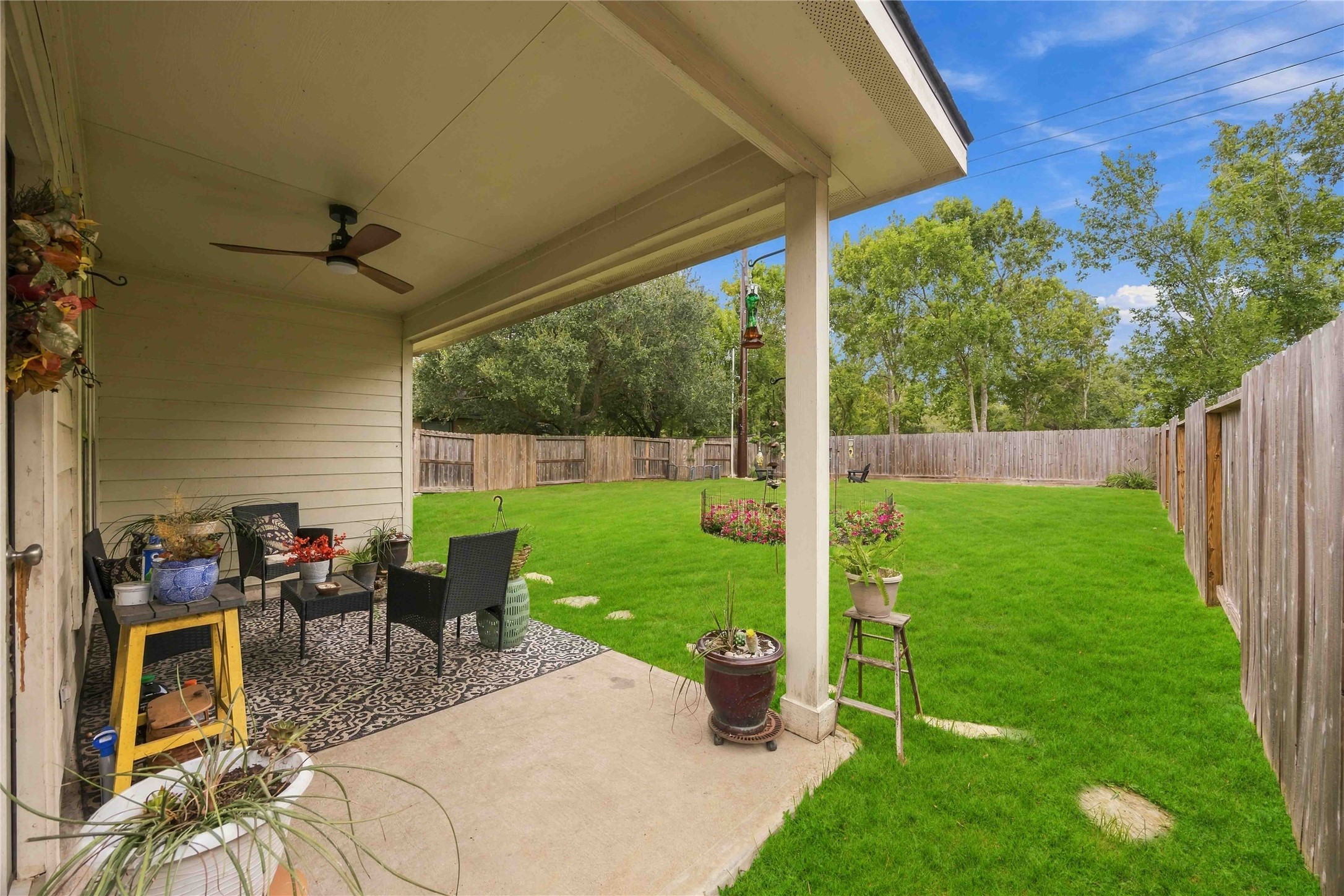 Covered back patio with a ceiling fan overlooking the expansive, fully fenced backyard.