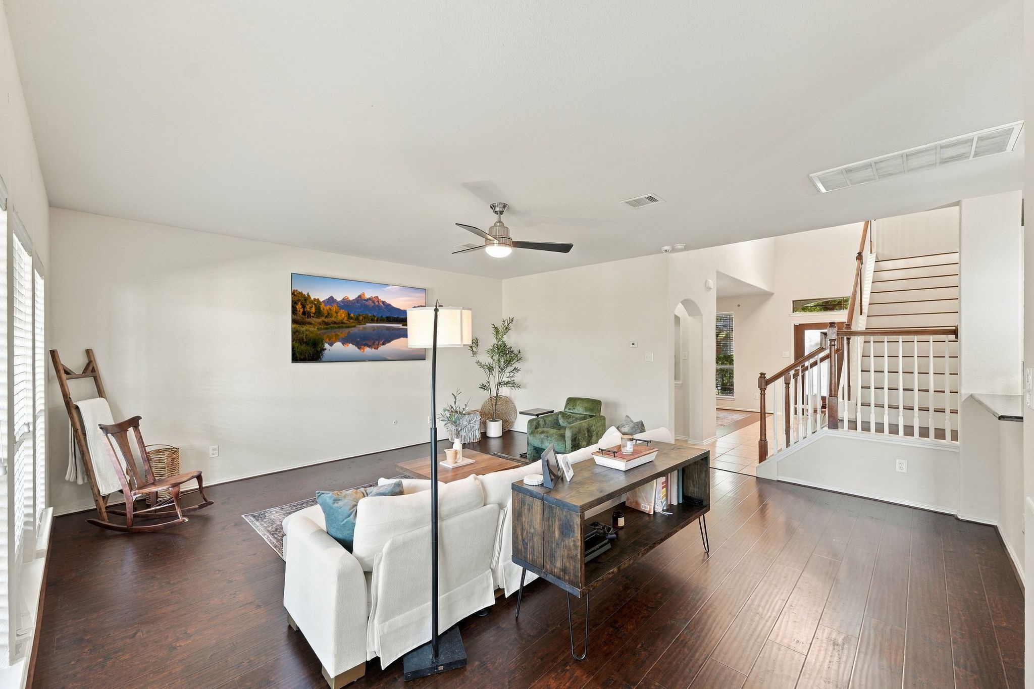 Spacious living room with elegant hardwood floors, abundant natural light, and a stylish ceiling fan, complemented by a modern staircase and cozy seating area.