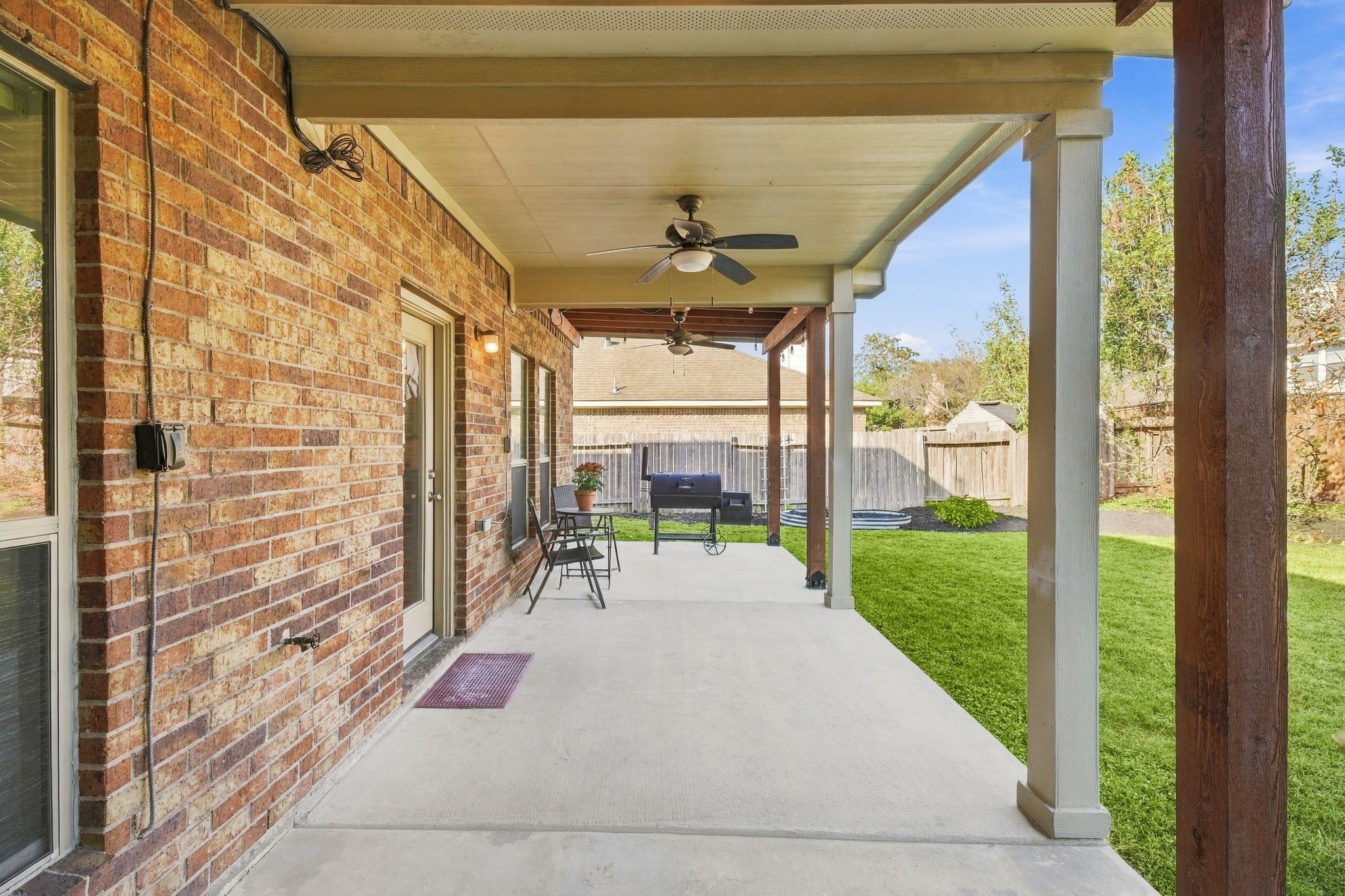 Spacious covered patio with ceiling fans, perfect for outdoor relaxation, overlooks a lush, well-maintained backyard.