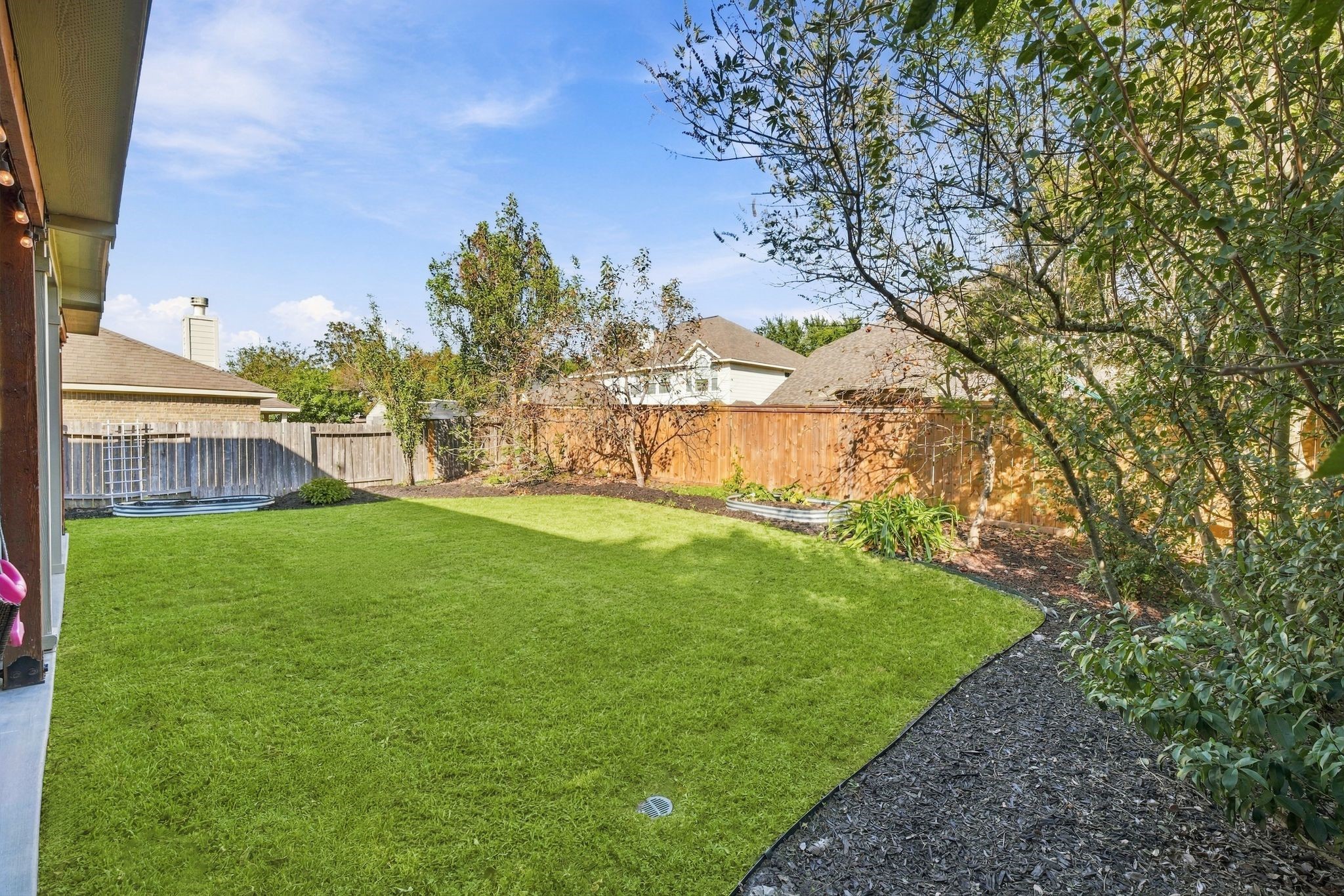 Spacious backyard with lush green lawn, mature trees, and wooden fencing, perfect for outdoor activities and privacy.