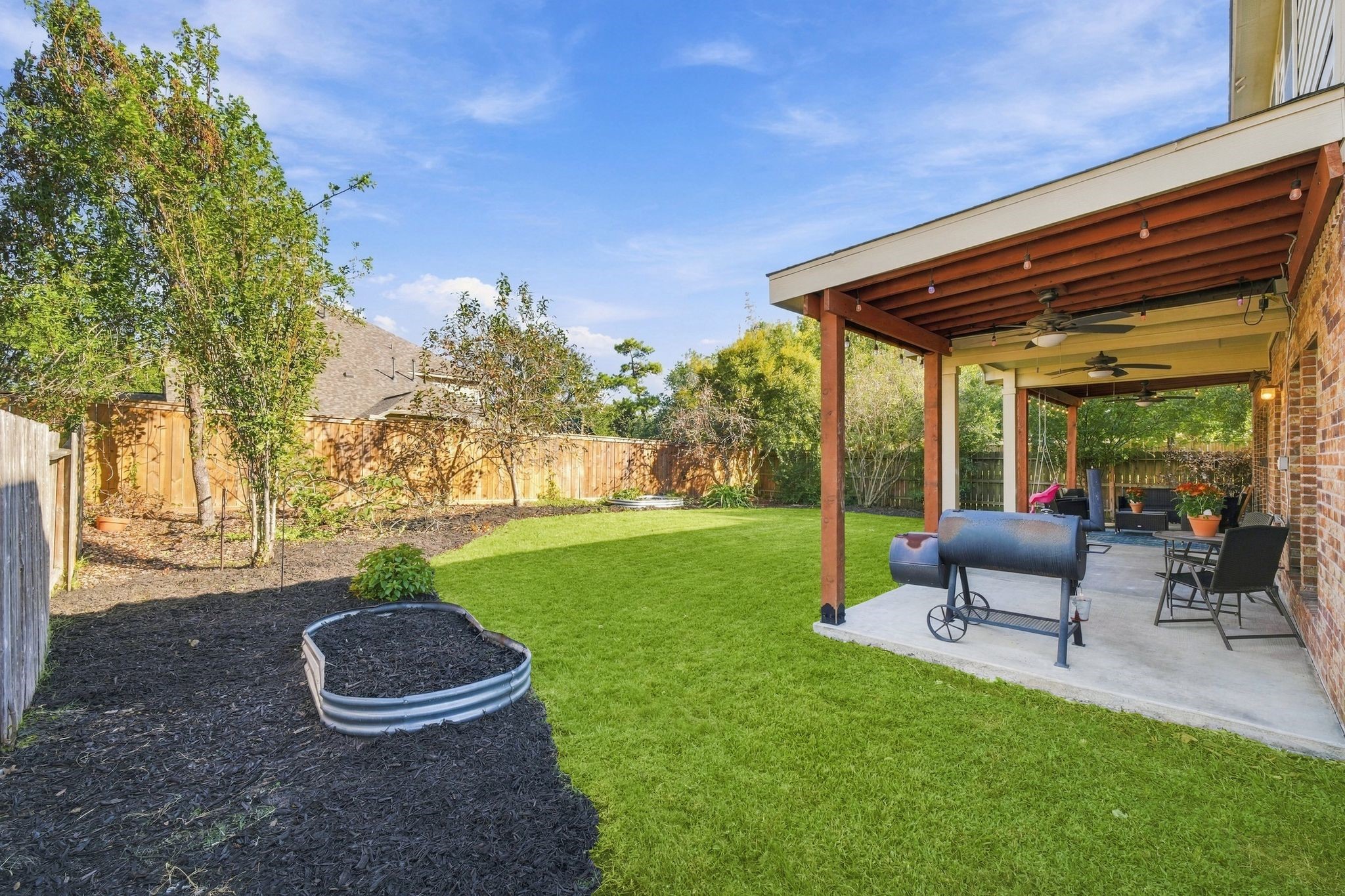 Spacious backyard featuring a covered patio with ceiling fans, perfect for outdoor gatherings, and a well-maintained lawn with surrounding greenery.