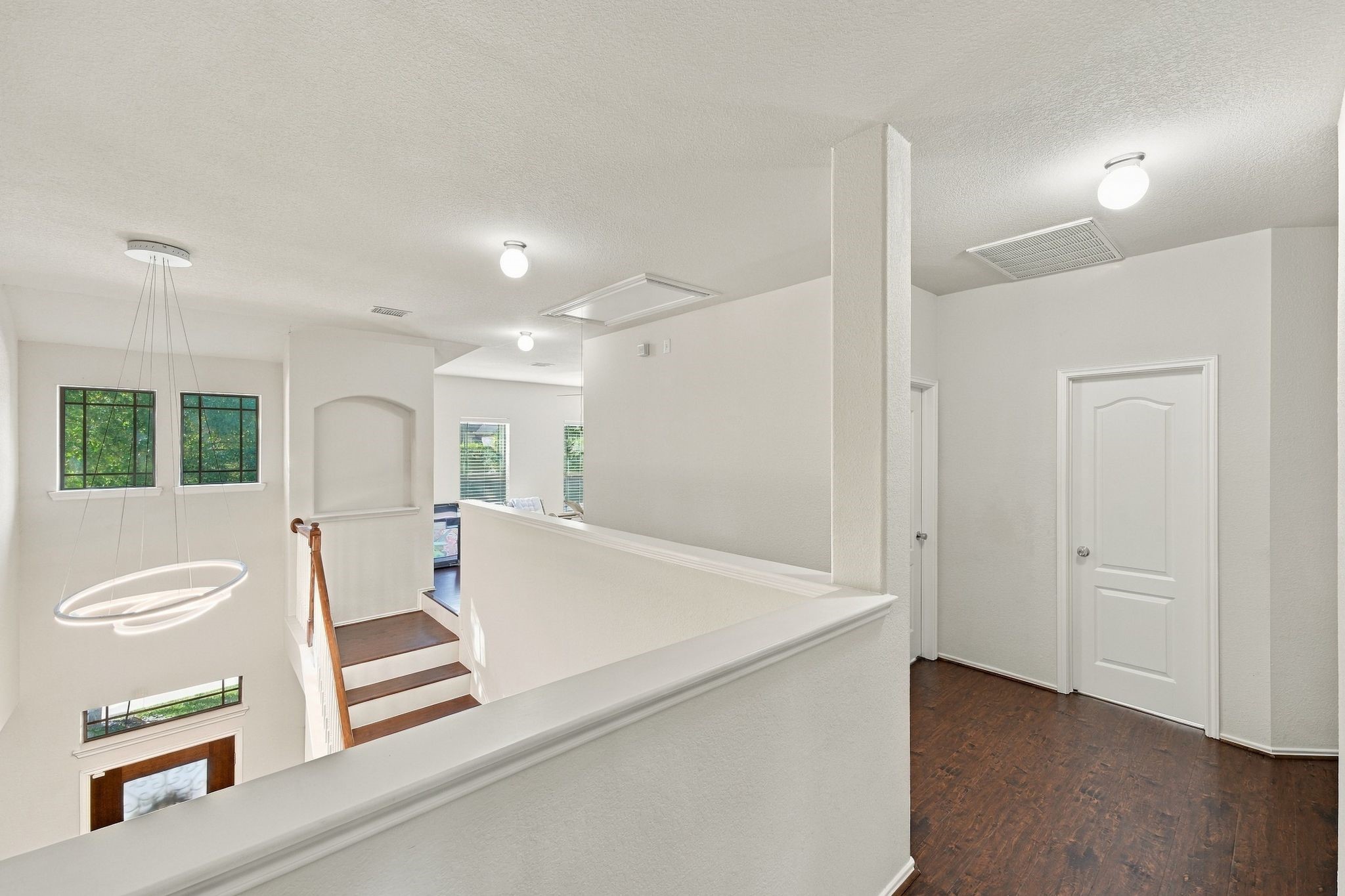 Bright and airy upstairs landing with modern lighting, elegant wood flooring, and multiple doorways leading to additional rooms.