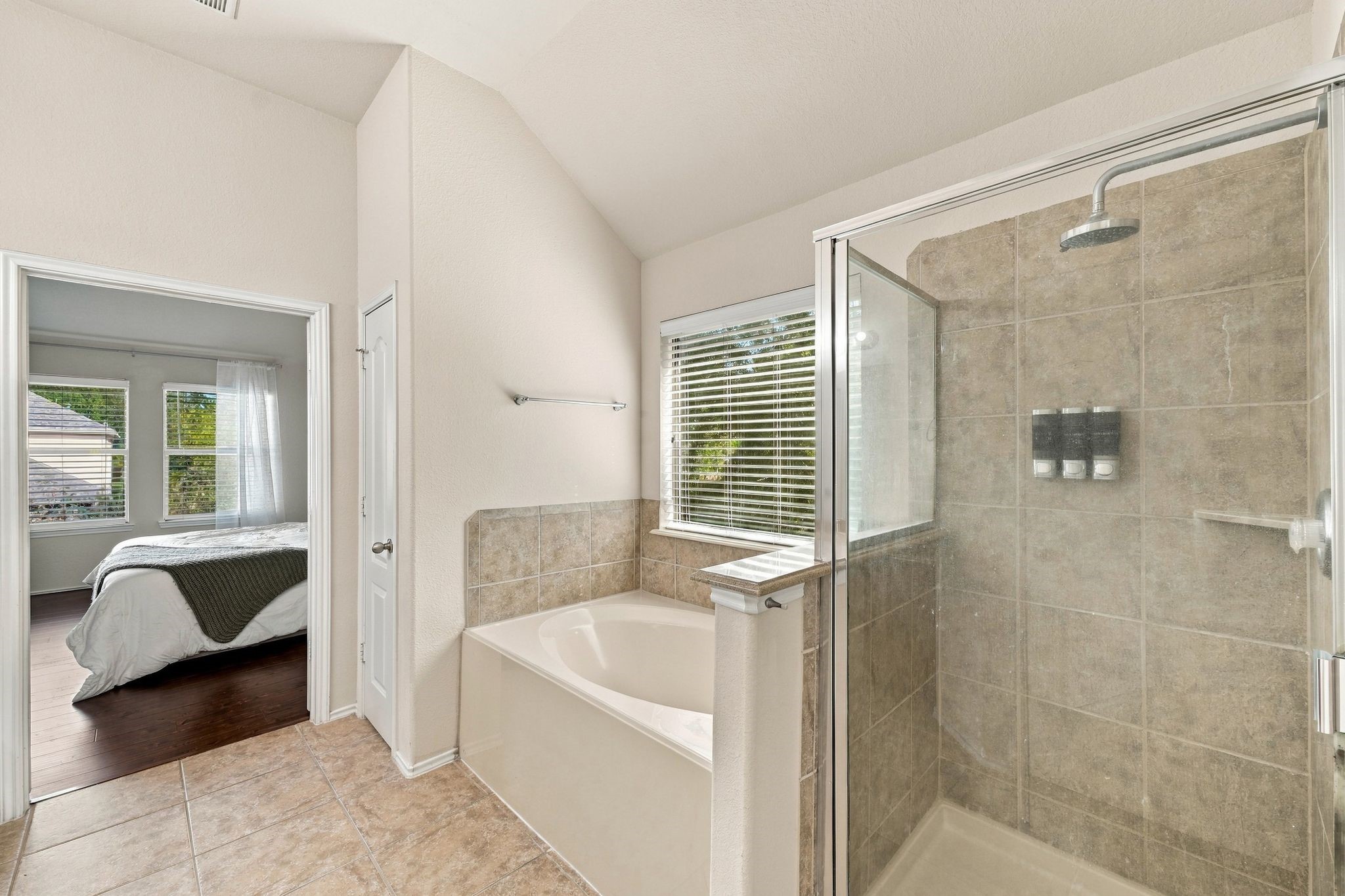 Bright primary bathroom featuring a spacious glass-enclosed shower, separate soaking tub, and tile flooring, with direct access to the primary bedroom.
