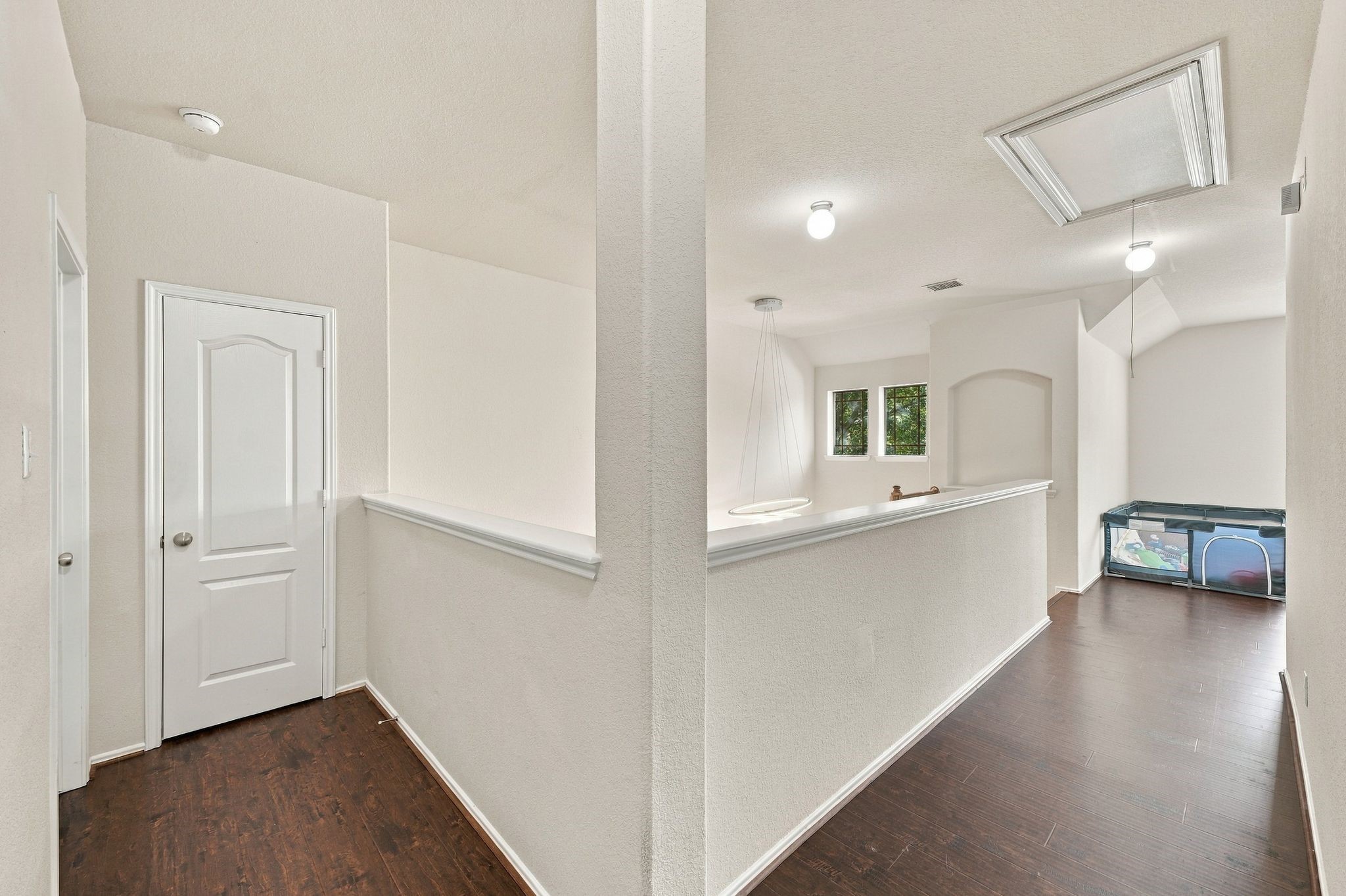 Bright upstairs hallway with dark wood flooring leads to a versatile open space perfect for a play area or lounge, featuring a storage closet and access to additional rooms.