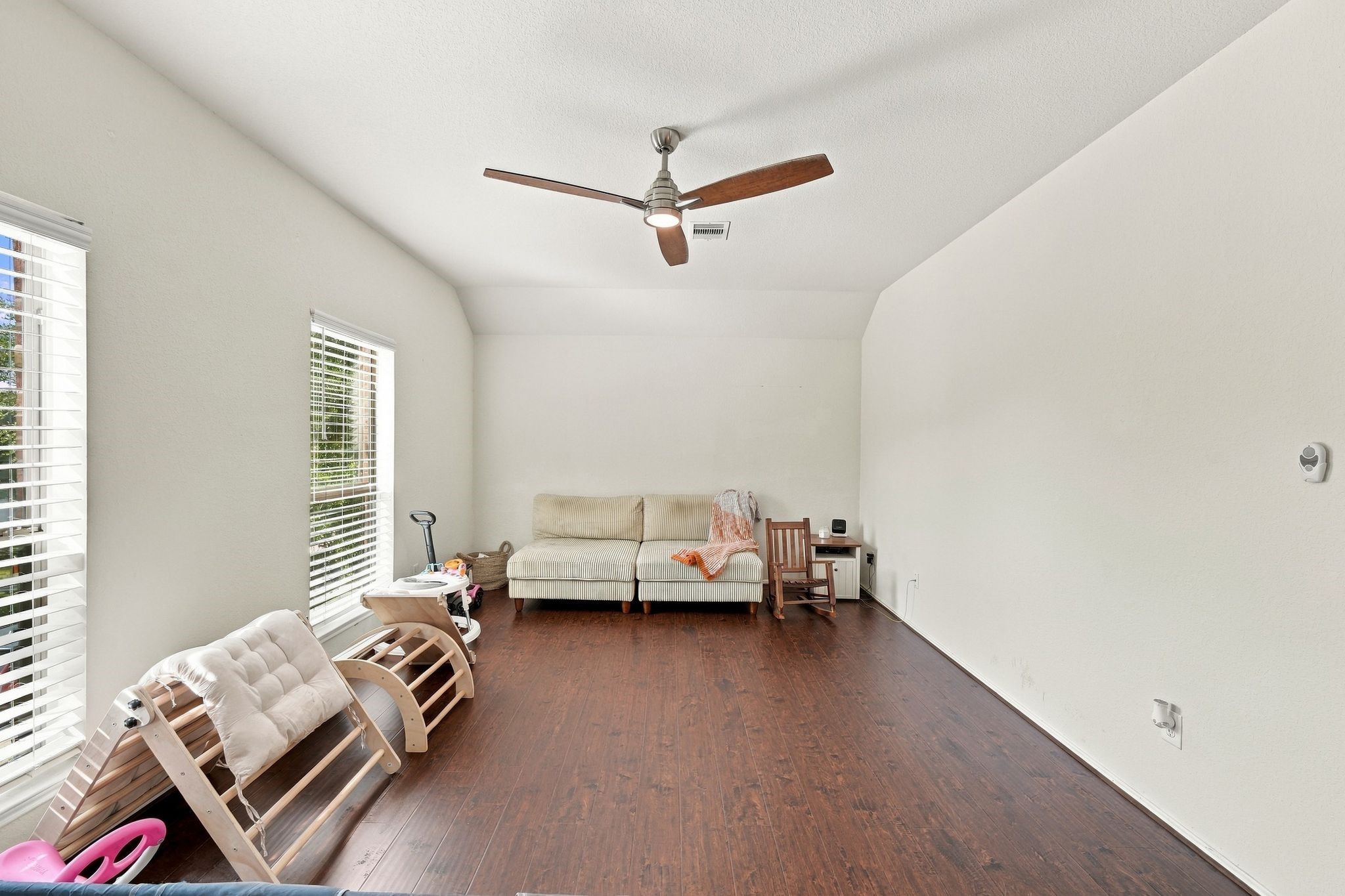Bright and spacious living area with elegant wood flooring, abundant natural light from large windows, and a stylish ceiling fan. This can also be used as upstairs game room
