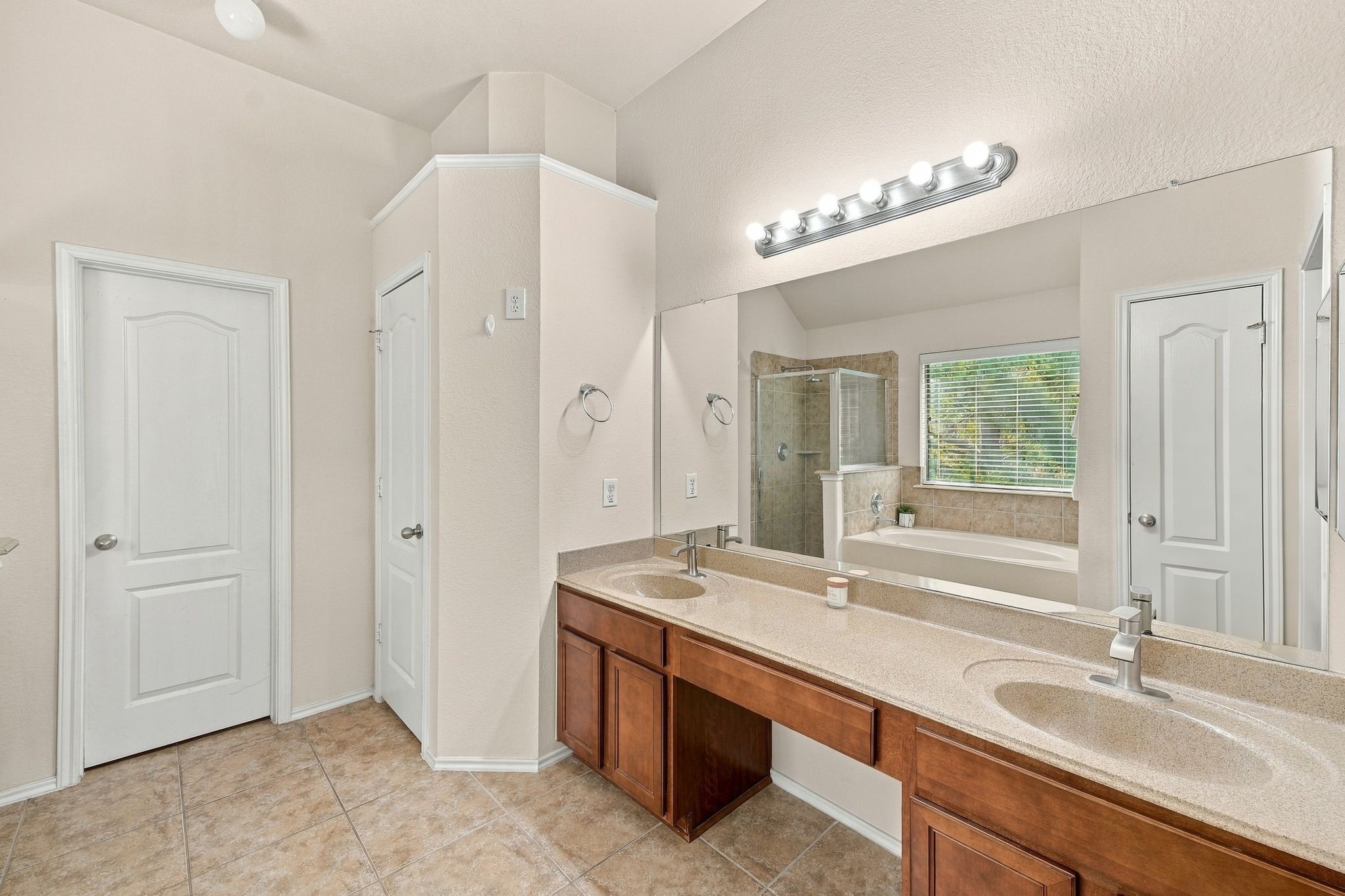 Spacious primary bathroom featuring a dual-sink vanity with elegant lighting, a large mirror, and a separate shower and bathtub for ultimate comfort.