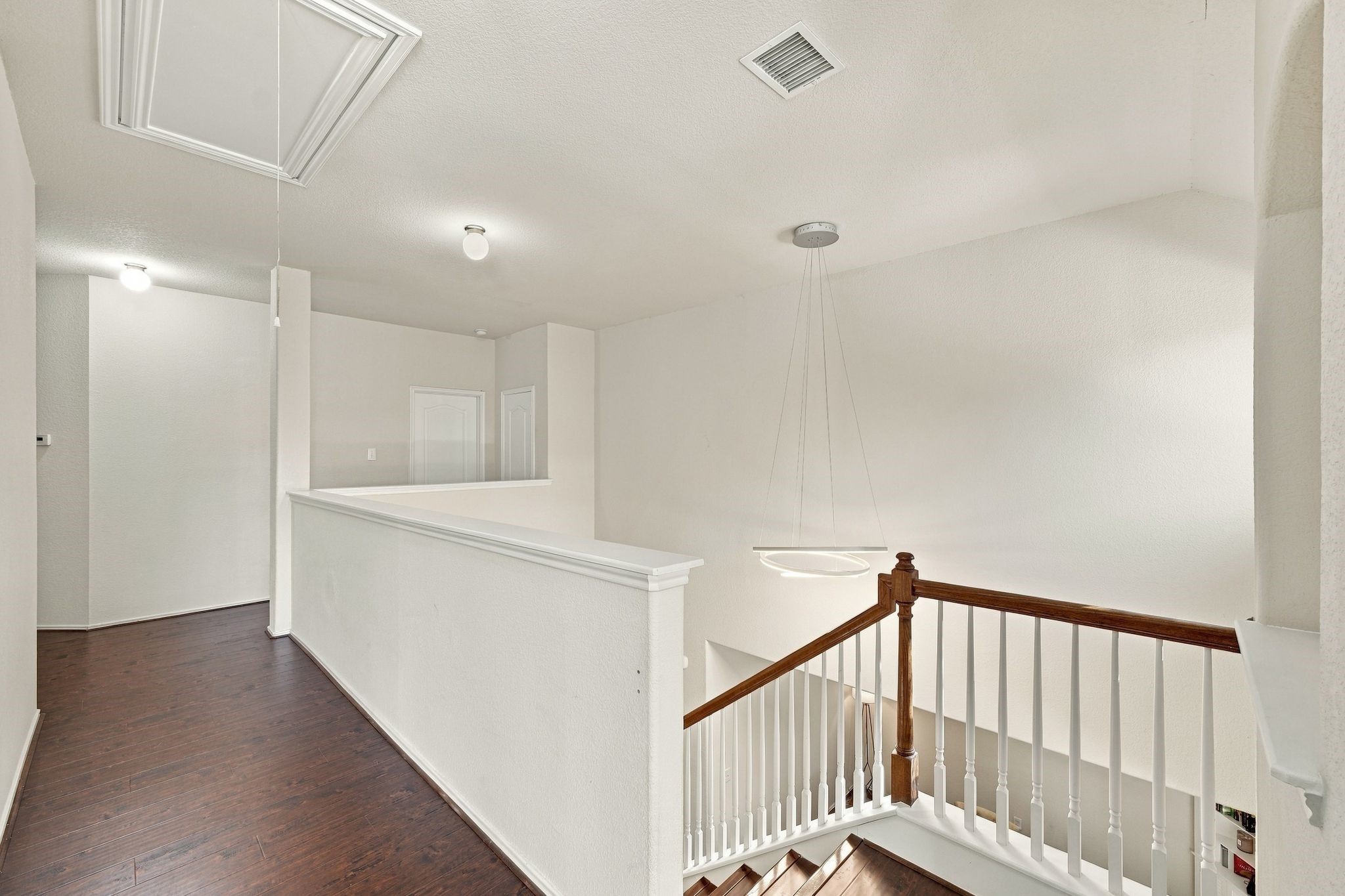 Bright and airy upstairs landing with elegant wood flooring and a modern light fixture, offering access to multiple rooms.