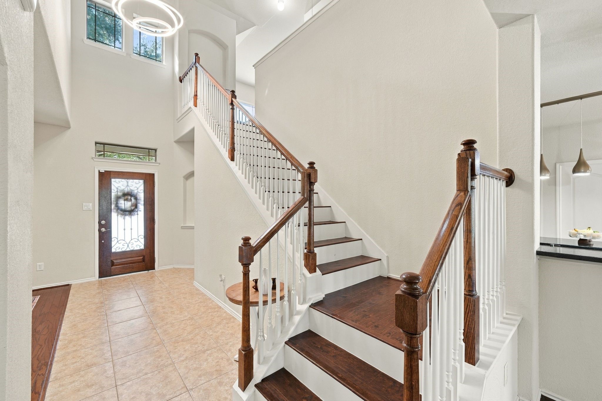 Elegant entryway with high ceilings, featuring a beautiful wooden staircase with white balusters and a stylish modern chandelier, creating a welcoming ambiance.