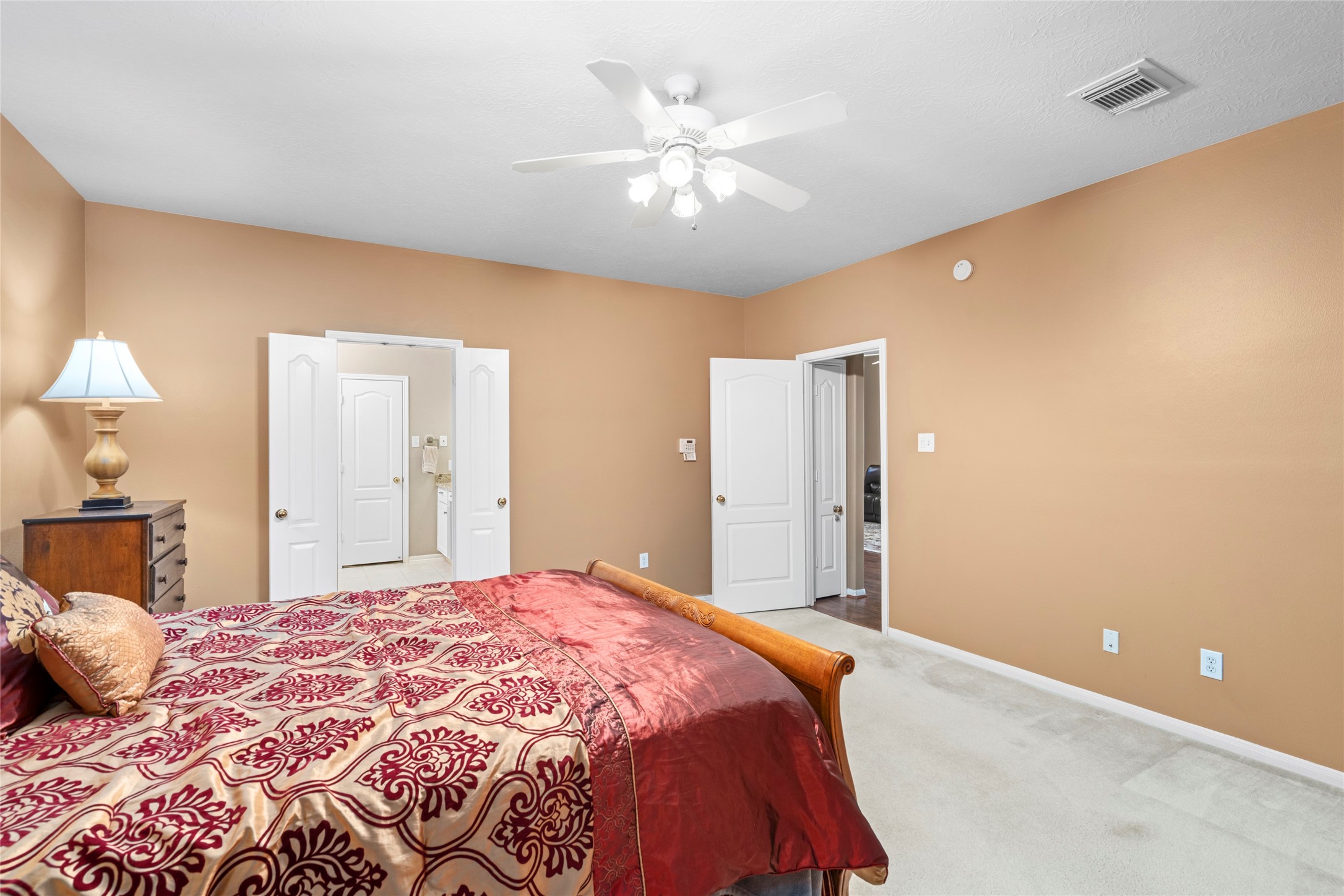 Comfortable bedroom with natural light, a ceiling fan, and a warm neutral setting that can easily adapt to different lifestyles. The room's proportions and double-door access offer flexibility for a bedroom, guest retreat, or personal space.