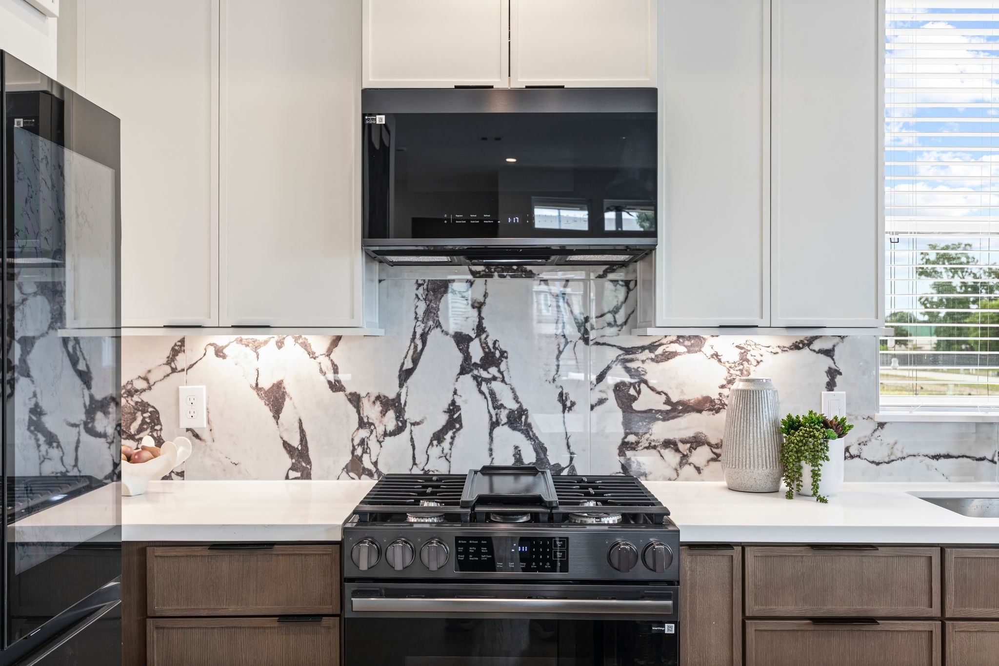 Sleek and modern kitchen featuring elegant marble-patterned backsplash, state-of-the-art appliances, and ample natural light for a sophisticated culinary experience. **Model Home of similar layout & finishes.** Sleek and modern kitchen featuring elegant marble-patterned backsplash, state-of-the-art appliances, and ample natural light for a sophisticated culinary experience. **Model Home of similar layout & finishes.**