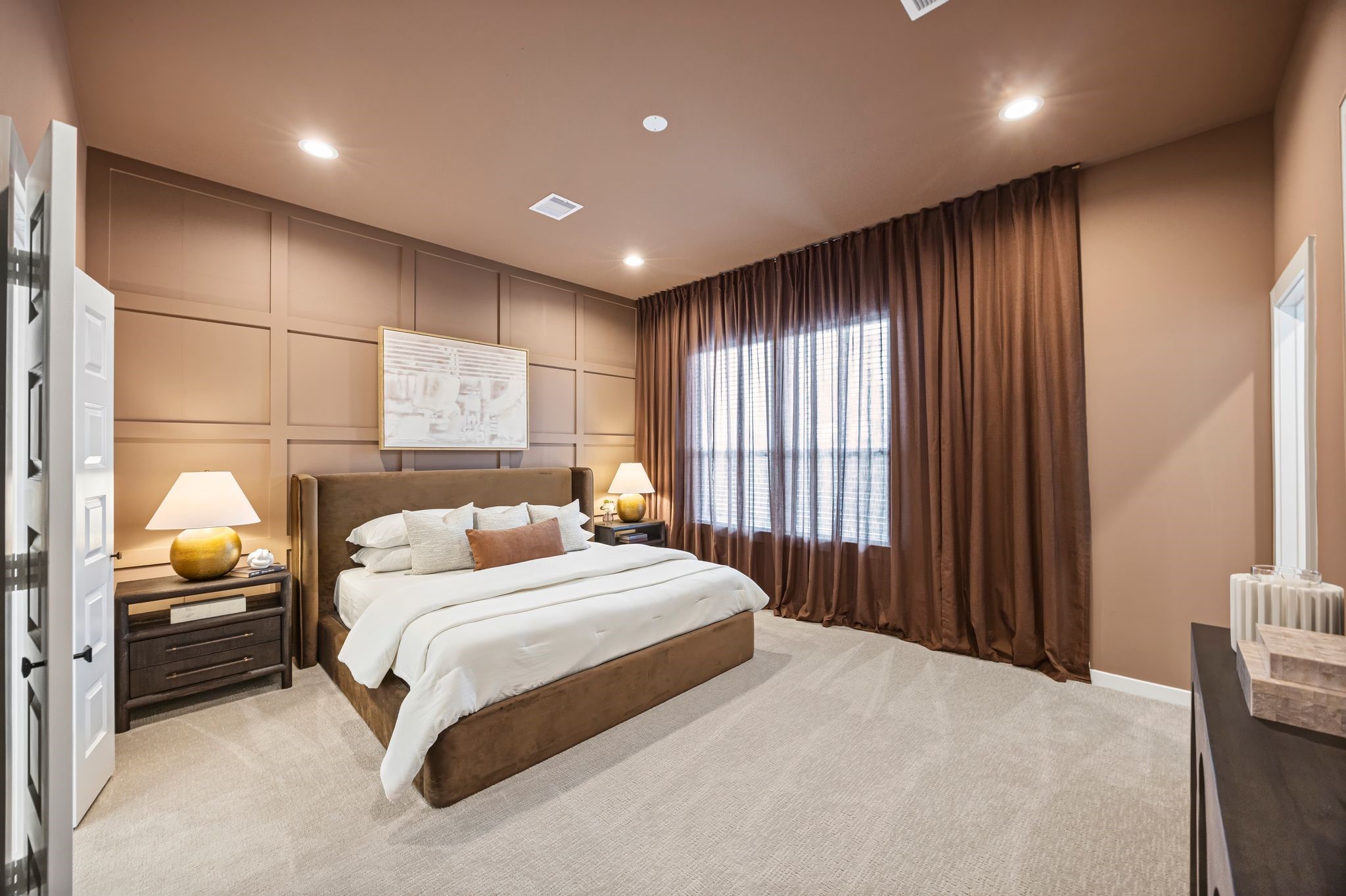 Experience serene elegance in the primary bedroom, featuring rich brown tones, plush carpeting, and soft lighting for a cozy retreat. **Model Home of similar layout & finishes.**