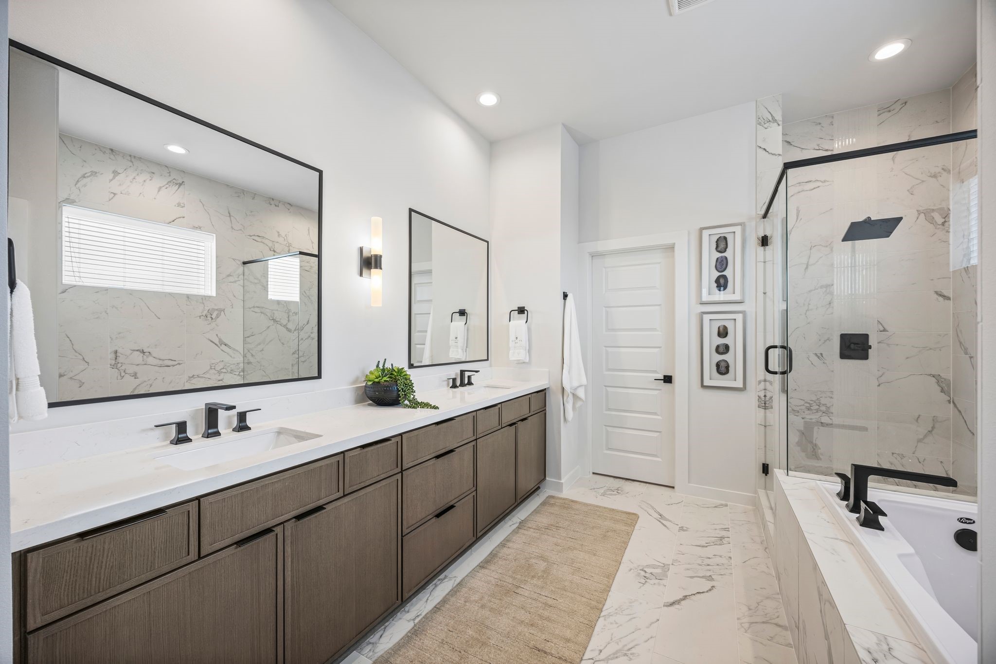 Experience modern luxury in this spacious primary bathroom, featuring dual vanities, elegant fixtures, and a glass-enclosed shower, all set against stylish marble accents. **Model Home of similar layout & finishes.**