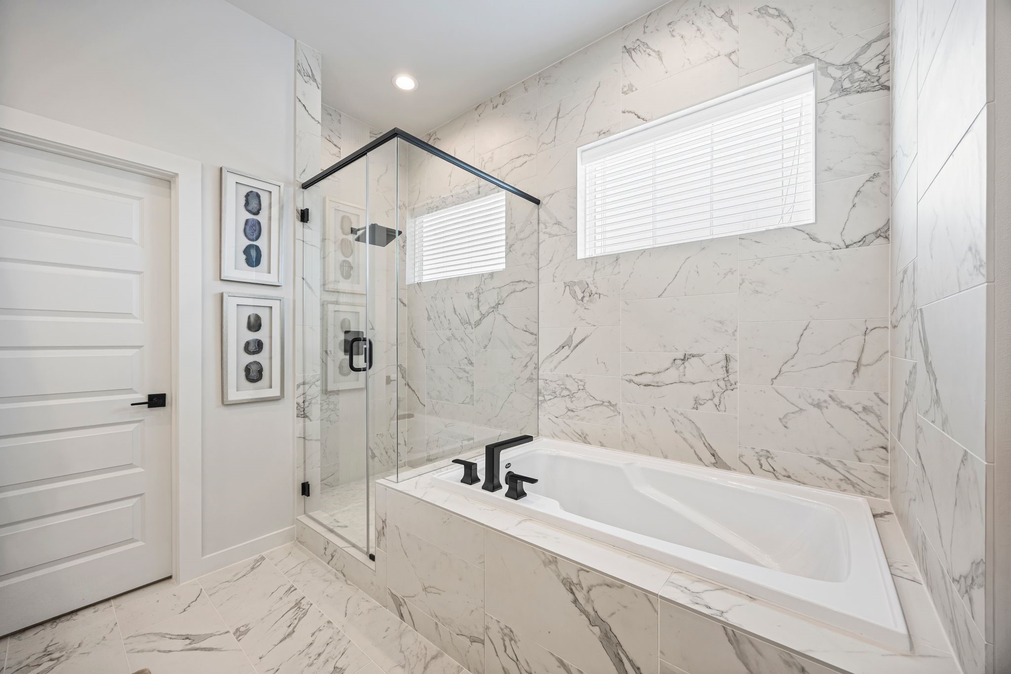 Experience luxury in the primary bathroom, featuring a sleek glass-enclosed shower and a sumptuous soaking tub, all set against elegant marble-patterned tiles. **Model Home of similar layout & finishes.**