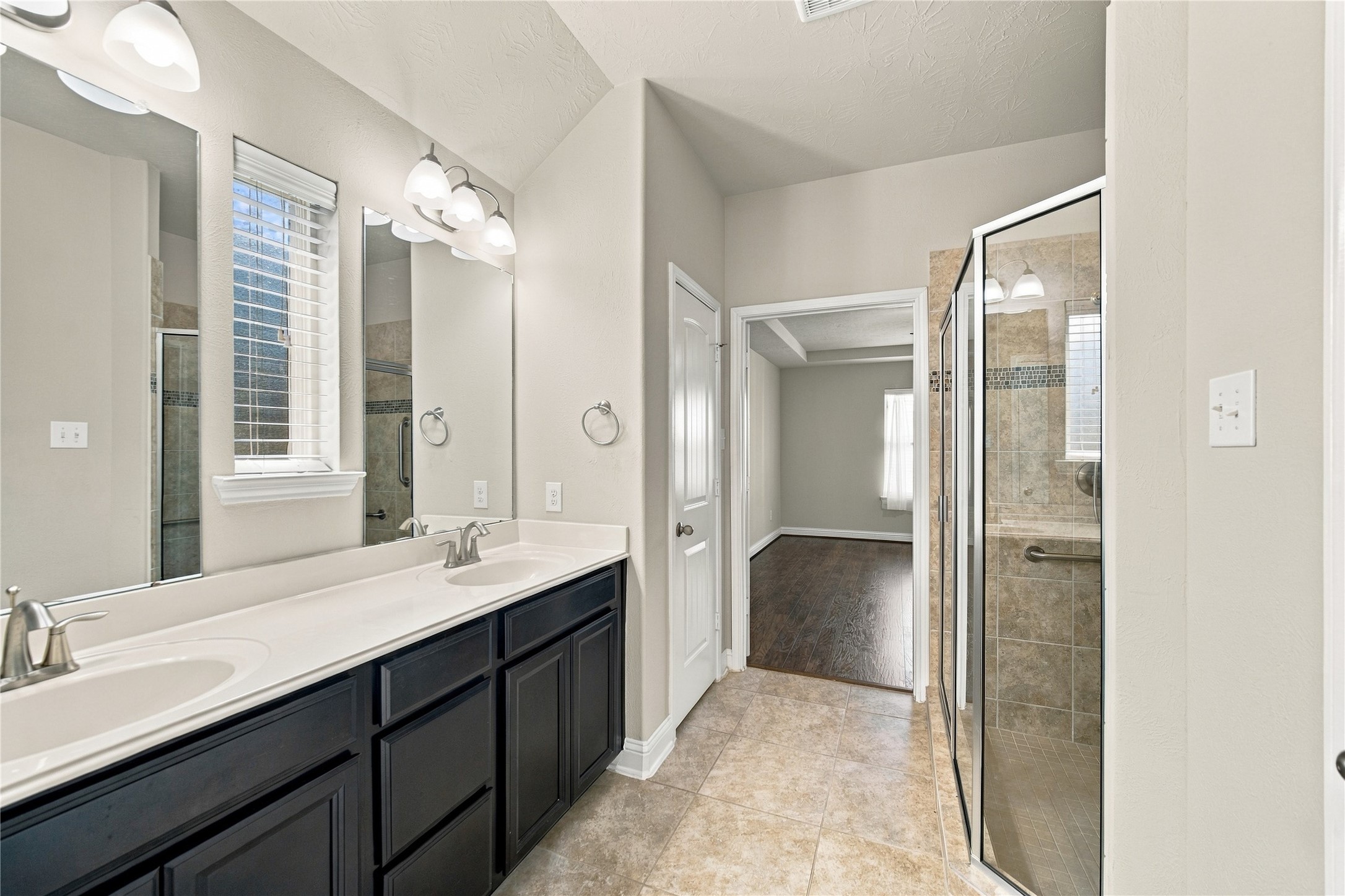 The primary ensuite features dual sinks with cabinetry and drawers for added storage, a glass-enclosed walk-in shower, and a convenient linen closet.