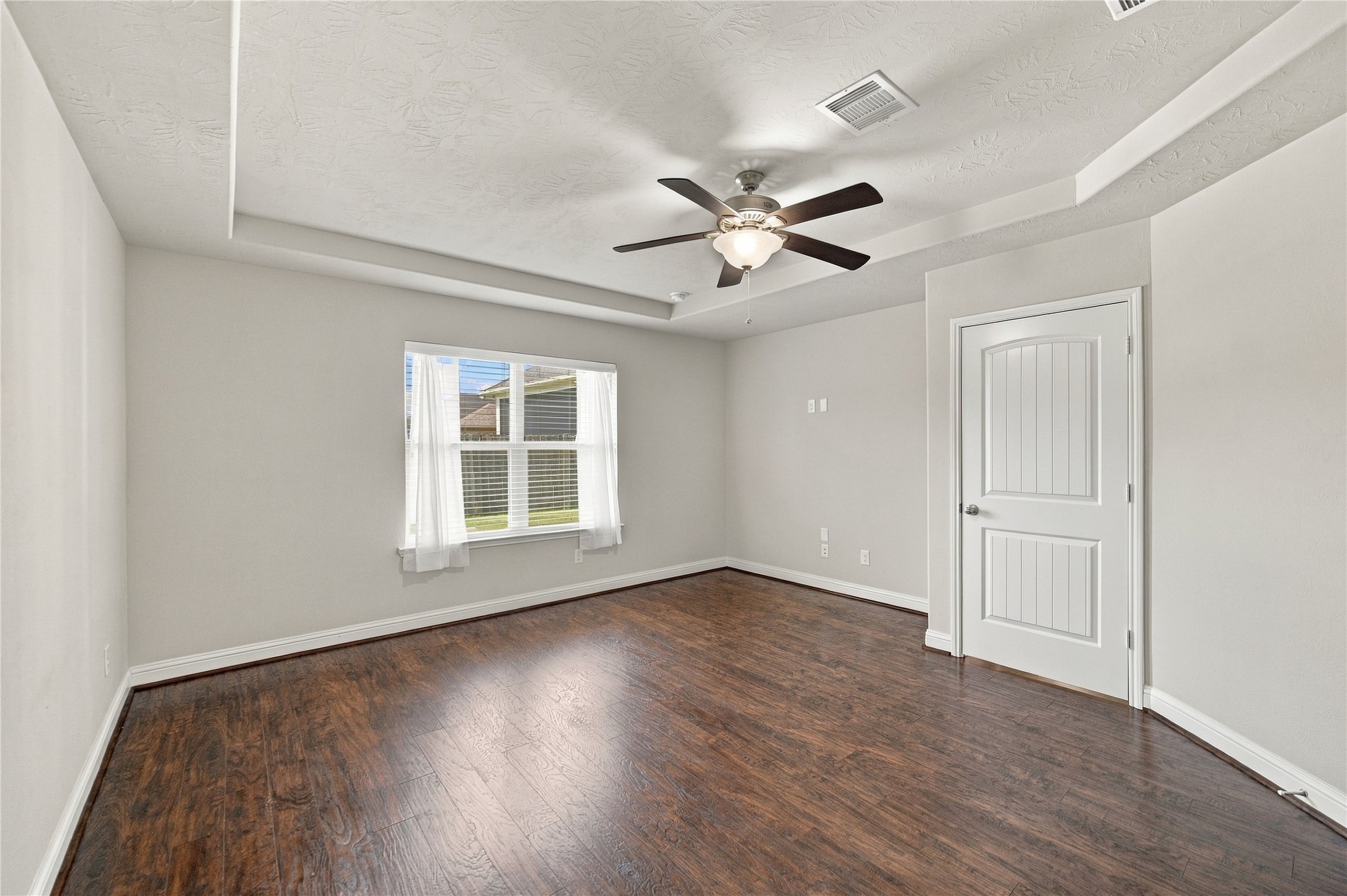 The beautiful wood flooring continues into the primary bedroom, where tray ceilings add architectural detail to the room.