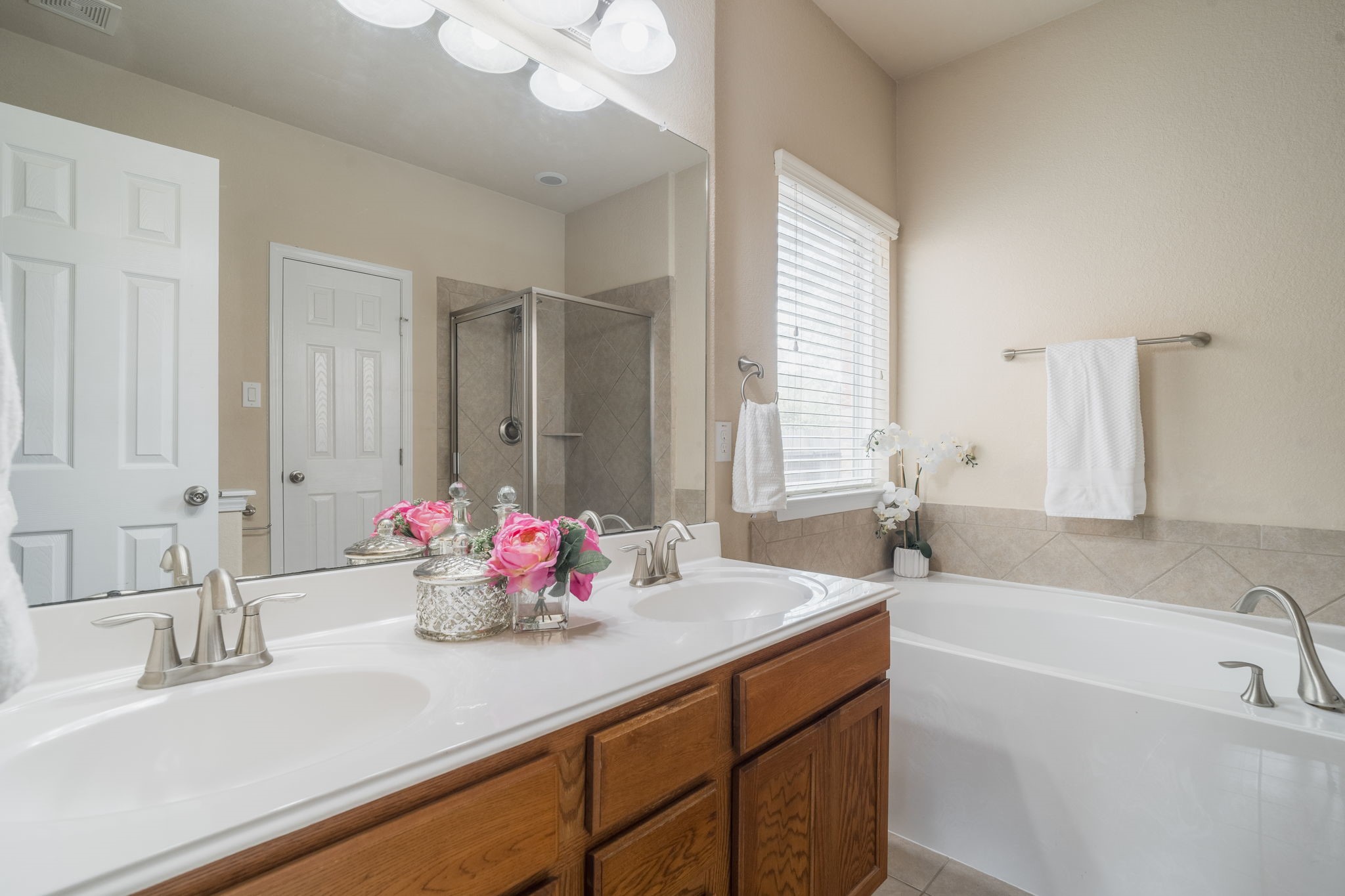 Primary en-suite bath featuring dual vanities, a soaking tub & a separate glass-enclosed shower with tile surround.
