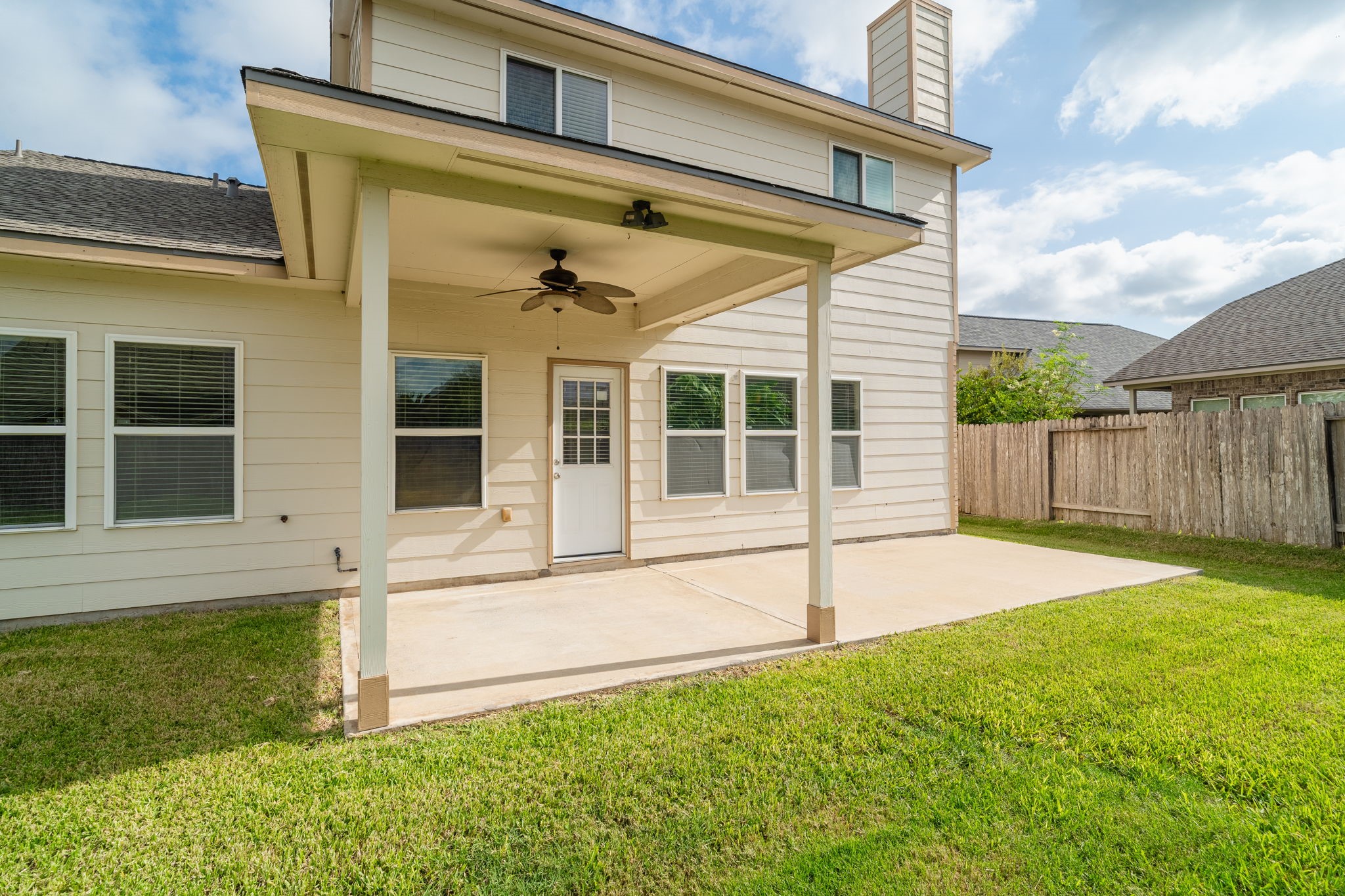 Generously sized covered patio with ceiling fan & an extended concrete area, offering flexibility for outdoor dining & seating.