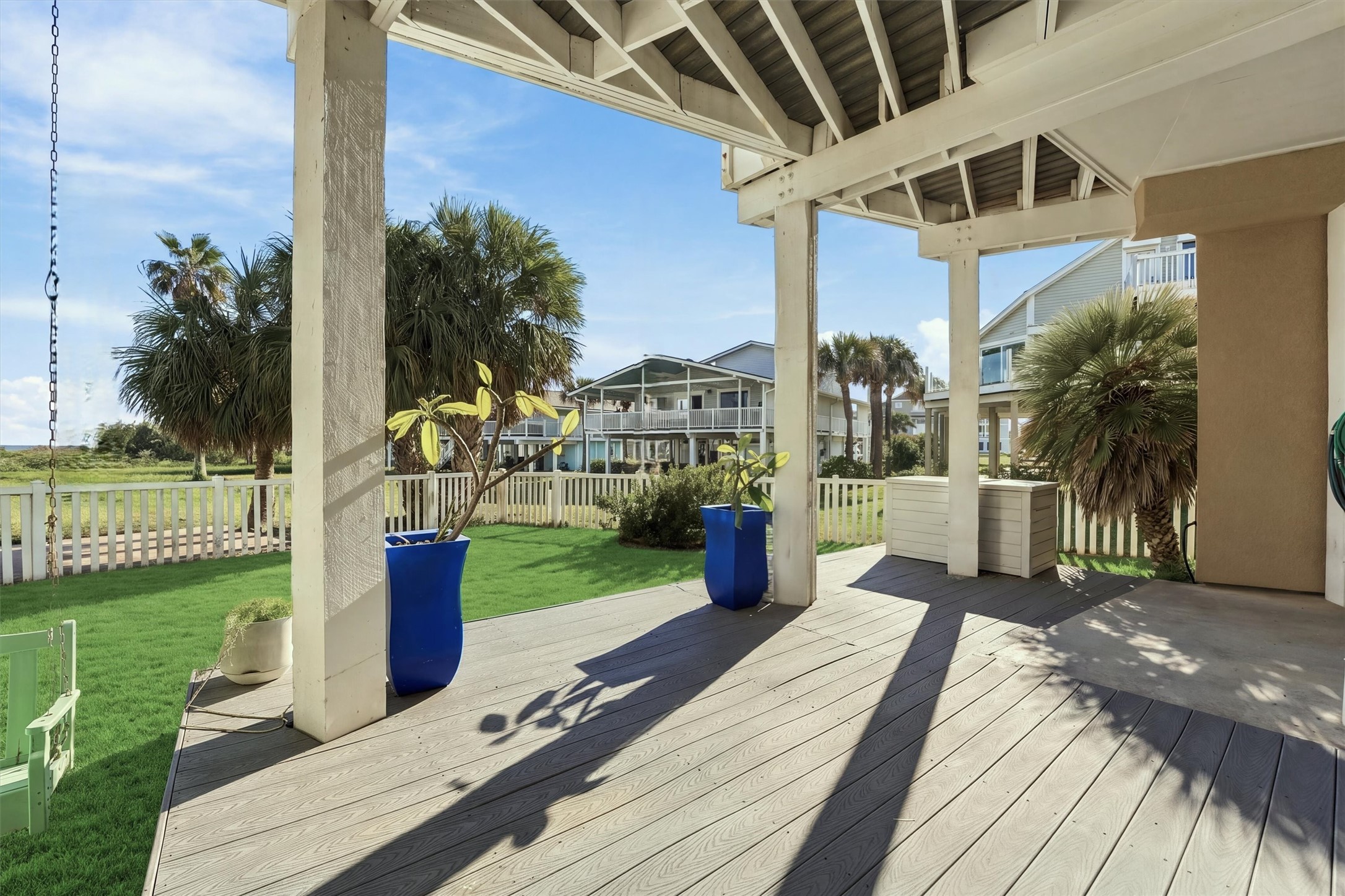 Step into the shade and enjoy a quiet moment overlooking the fenced lawn. Potted plumerias and surrounding palms bring tropical charm to this covered outdoor retreat, with the beach just steps away.