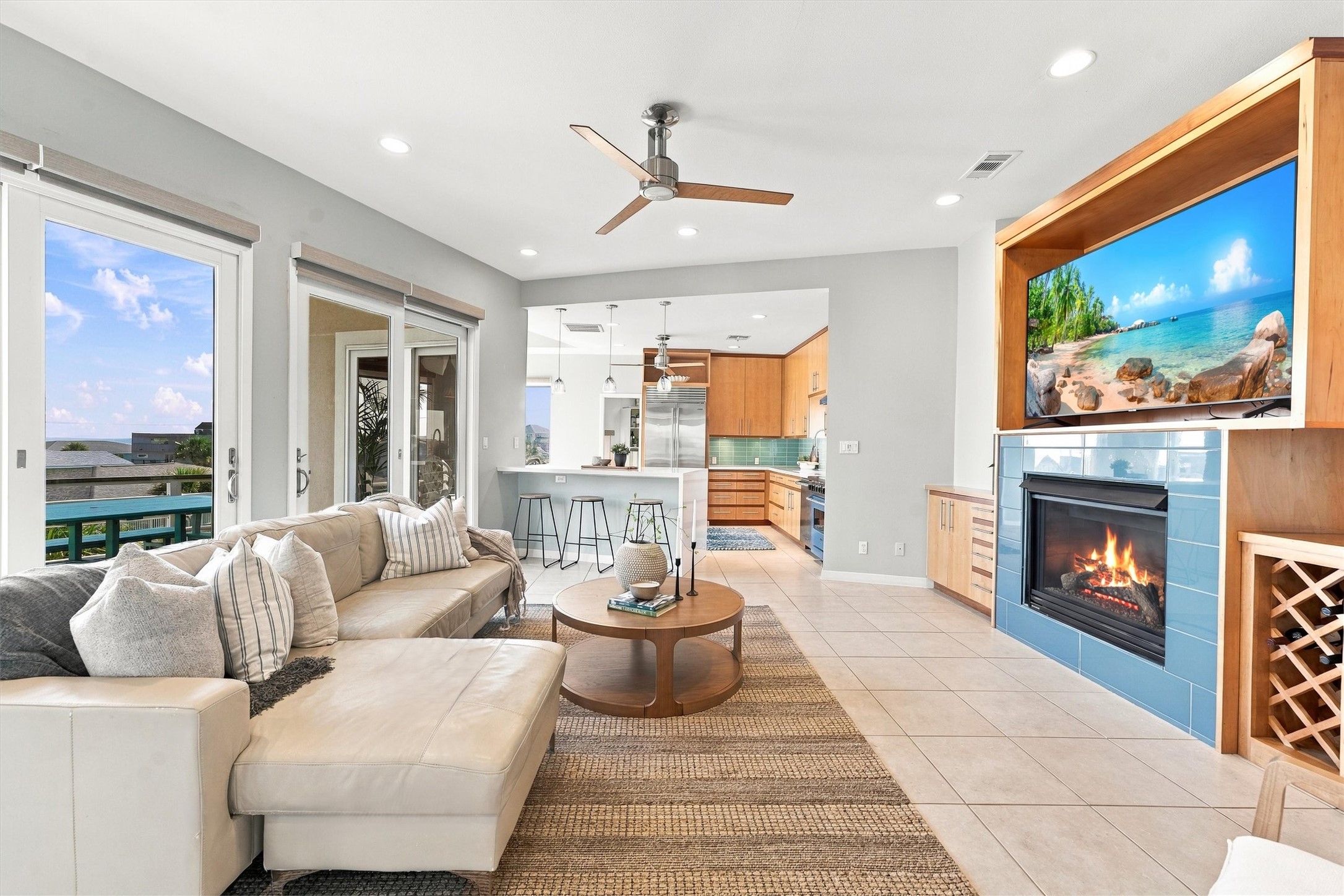Spend the afternoon by the water, then settle into this light-filled living area. A blue-tiled fireplace adds warmth, while sliding glass doors connect the gathering space to balcony dining and coastal views.