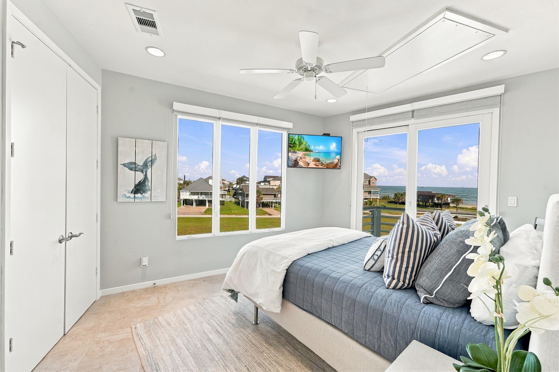 Wake to blue skies and the water stretching toward the horizon. Tall windows and sliding glass doors fill this bedroom with natural light, offering a daily reminder that the beach is only steps away.